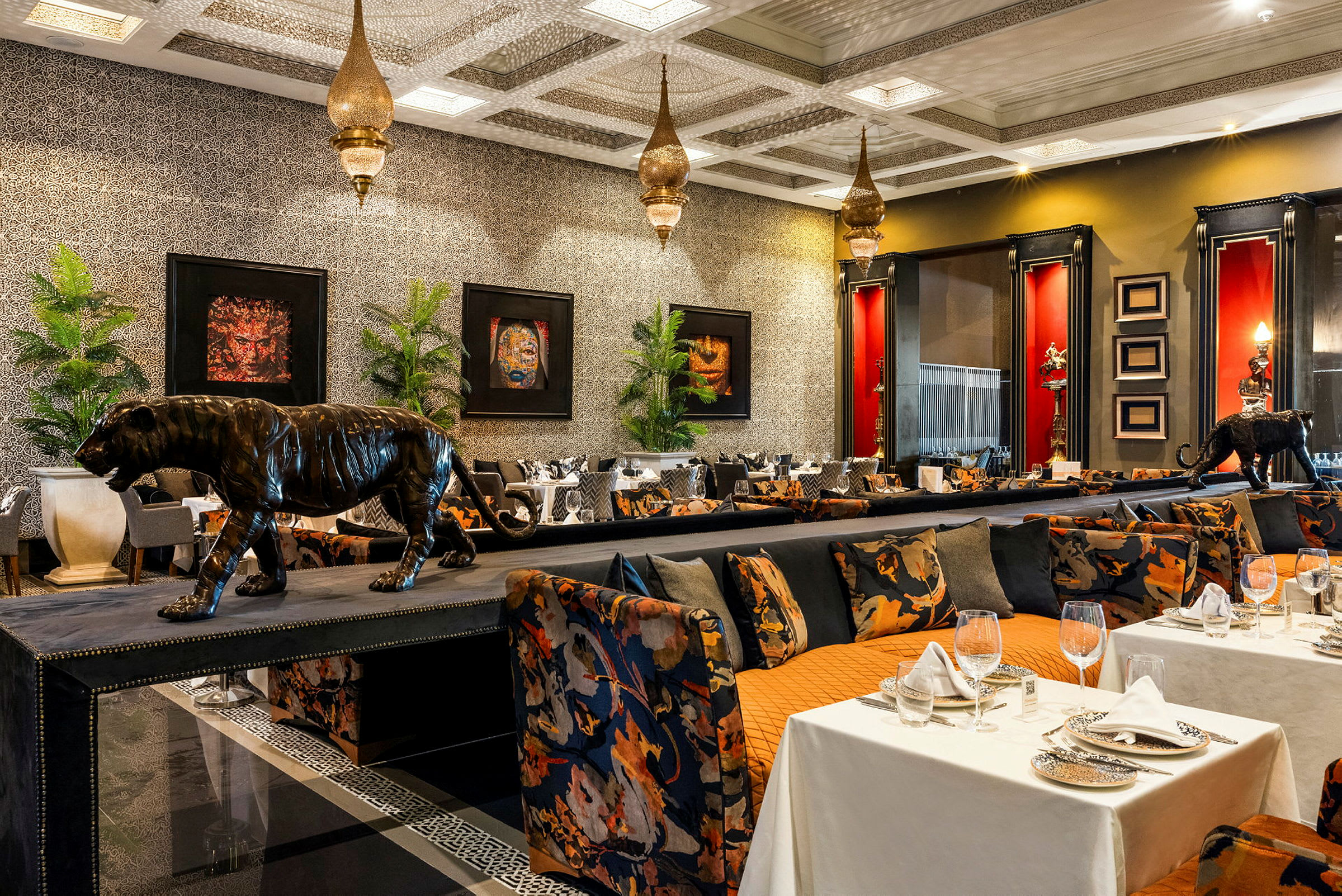 Bild av en elegant restaurang med exotiskt tema, inklusive dekorationer av leopardstatyer, förgyllda lampor och färgrika möbler. (AI-genererad text)