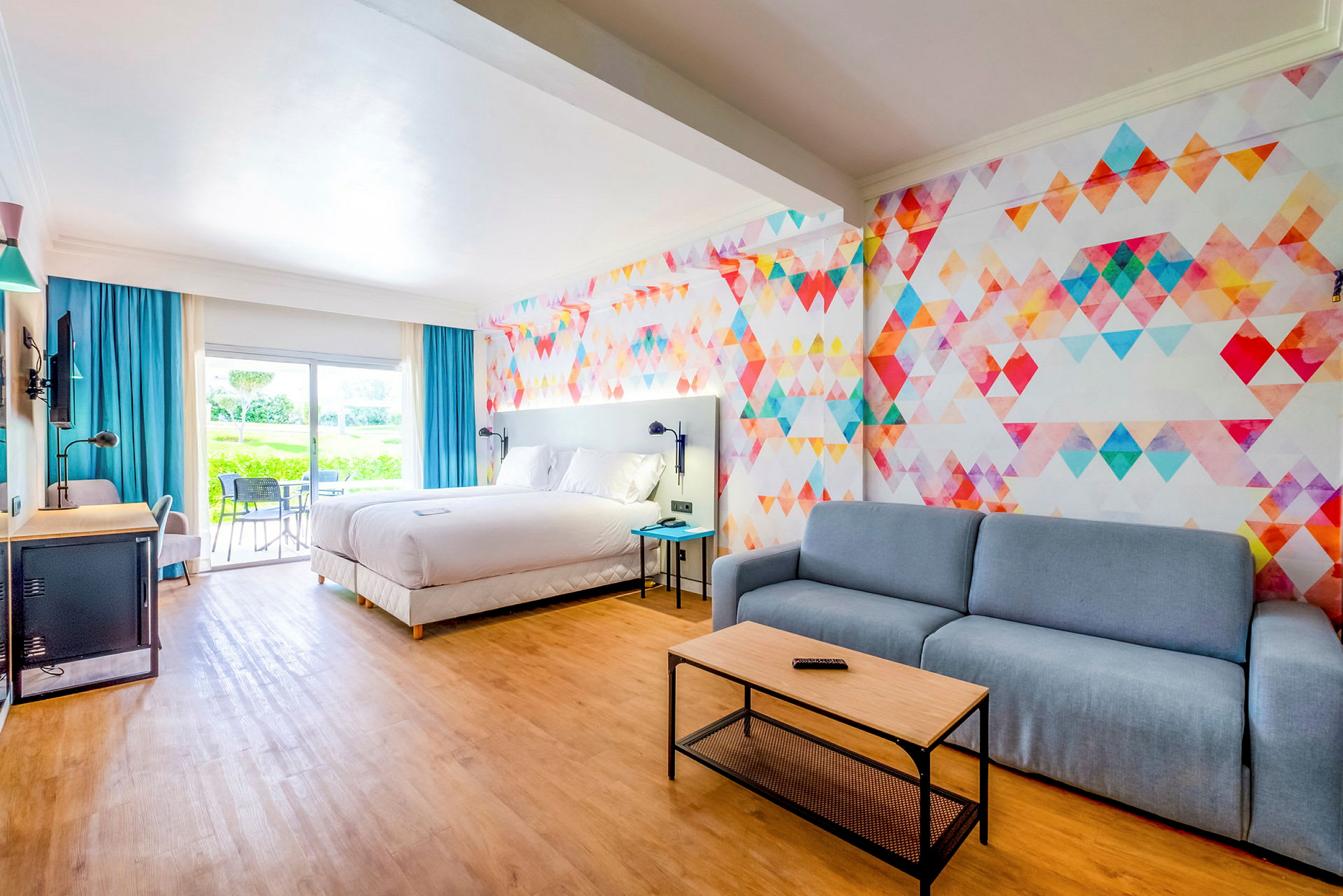 Hotellrum med stor säng, sittgrupp och färgglad väggdesign. (AI-genererad text)