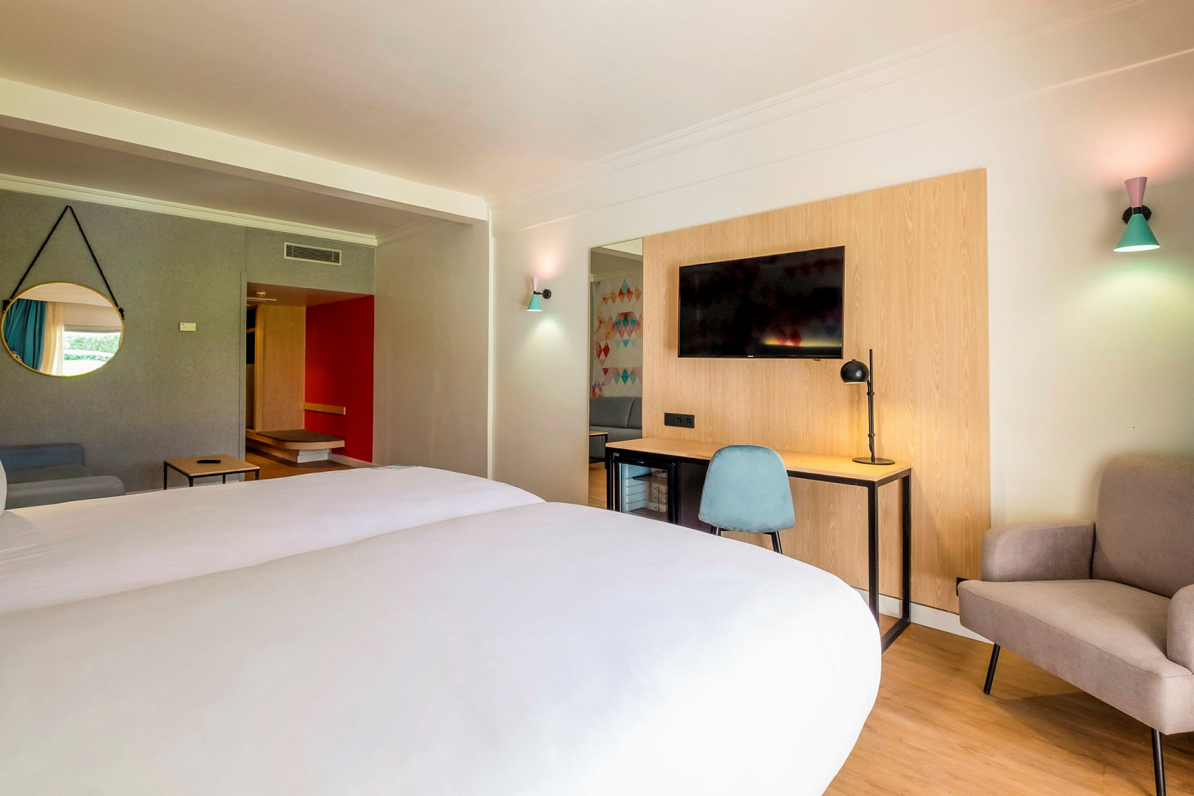 Hotellrum med dubbelsäng, skrivbord och stol, TV samt sittplats. (AI-genererad text)