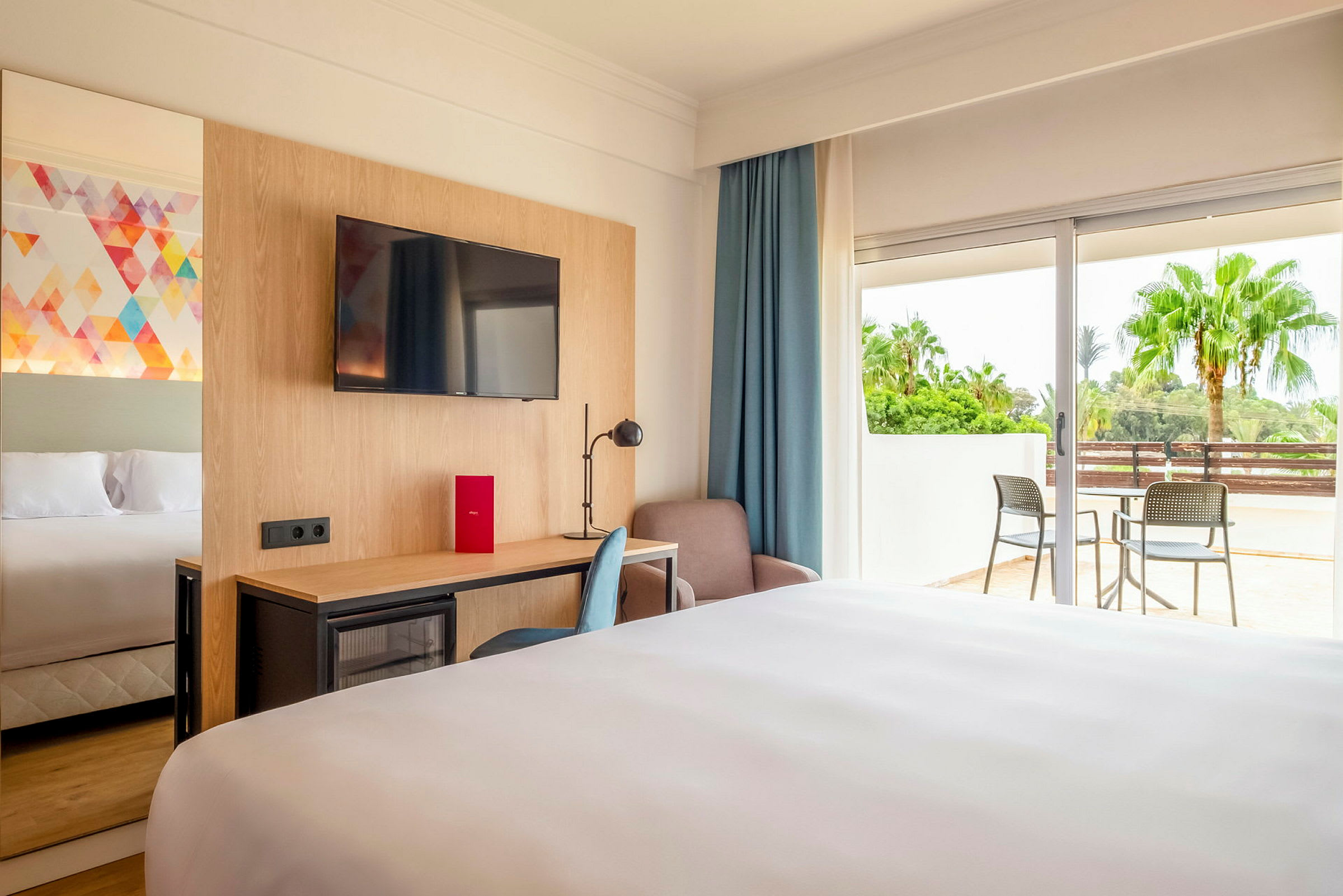 Ett hotellrum med dubbelsäng, TV, skrivbord och balkong. (AI-genererad text)