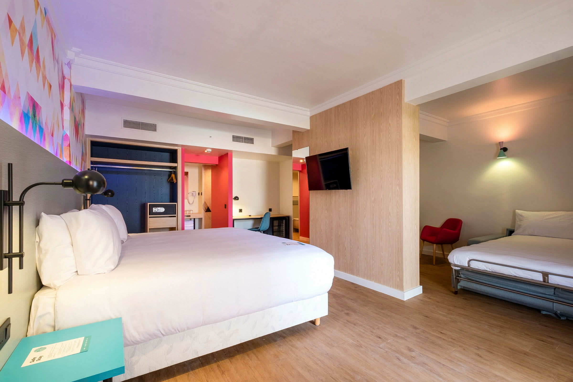 Ett hotellrum med två sängar, en TV på väggen och färgglada detaljer. (AI-genererad text)