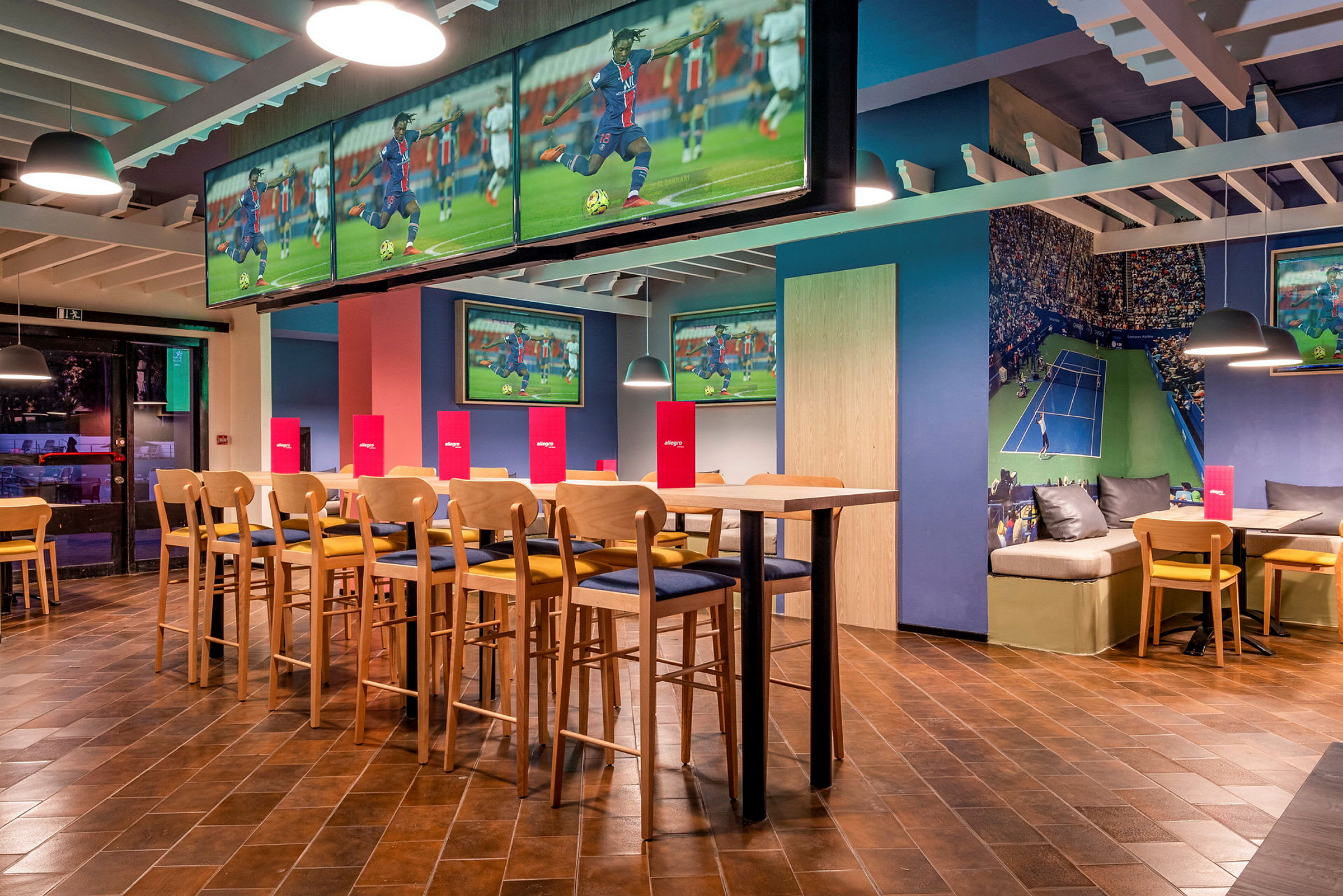 Interiör av en sportbar med tv-skärmar som visar fotboll och tennis, sittplatser och bord. (AI-genererad text)