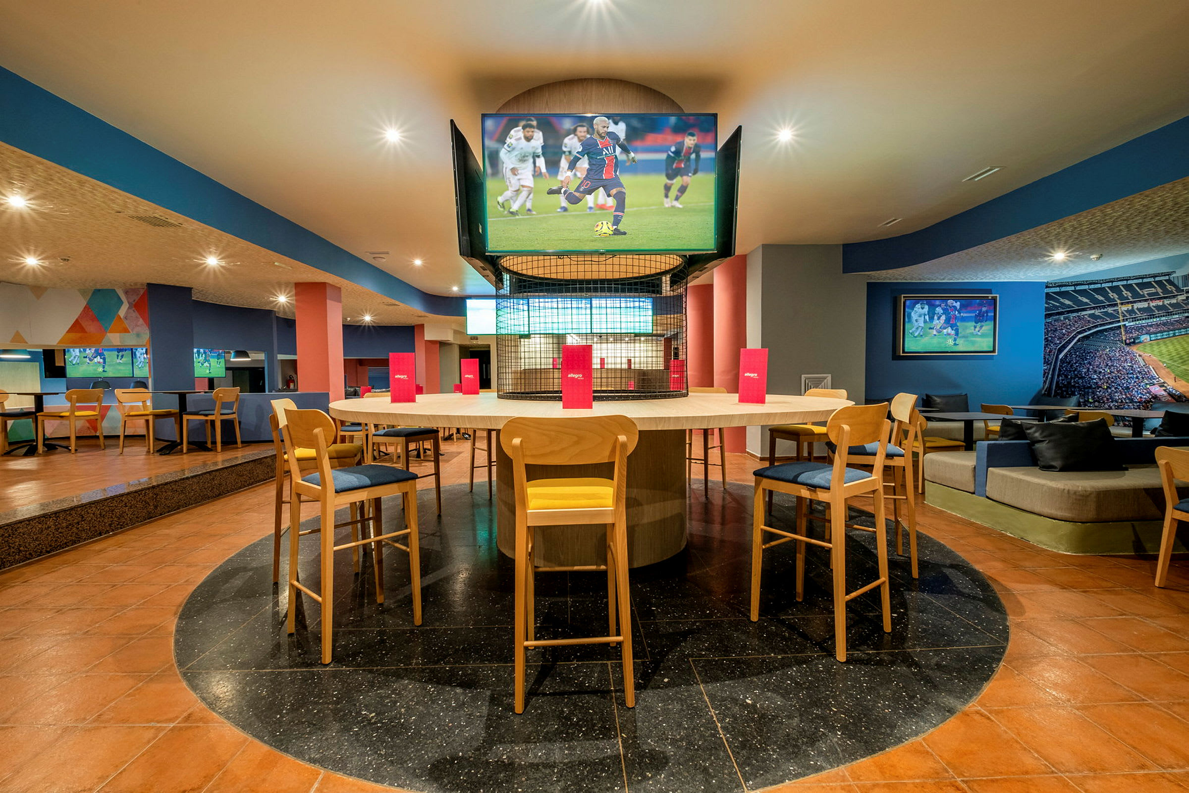 Interiör av ett modernt sportbar med sittplatser kring ett bord och flera TV-skärmar. (AI-genererad text)