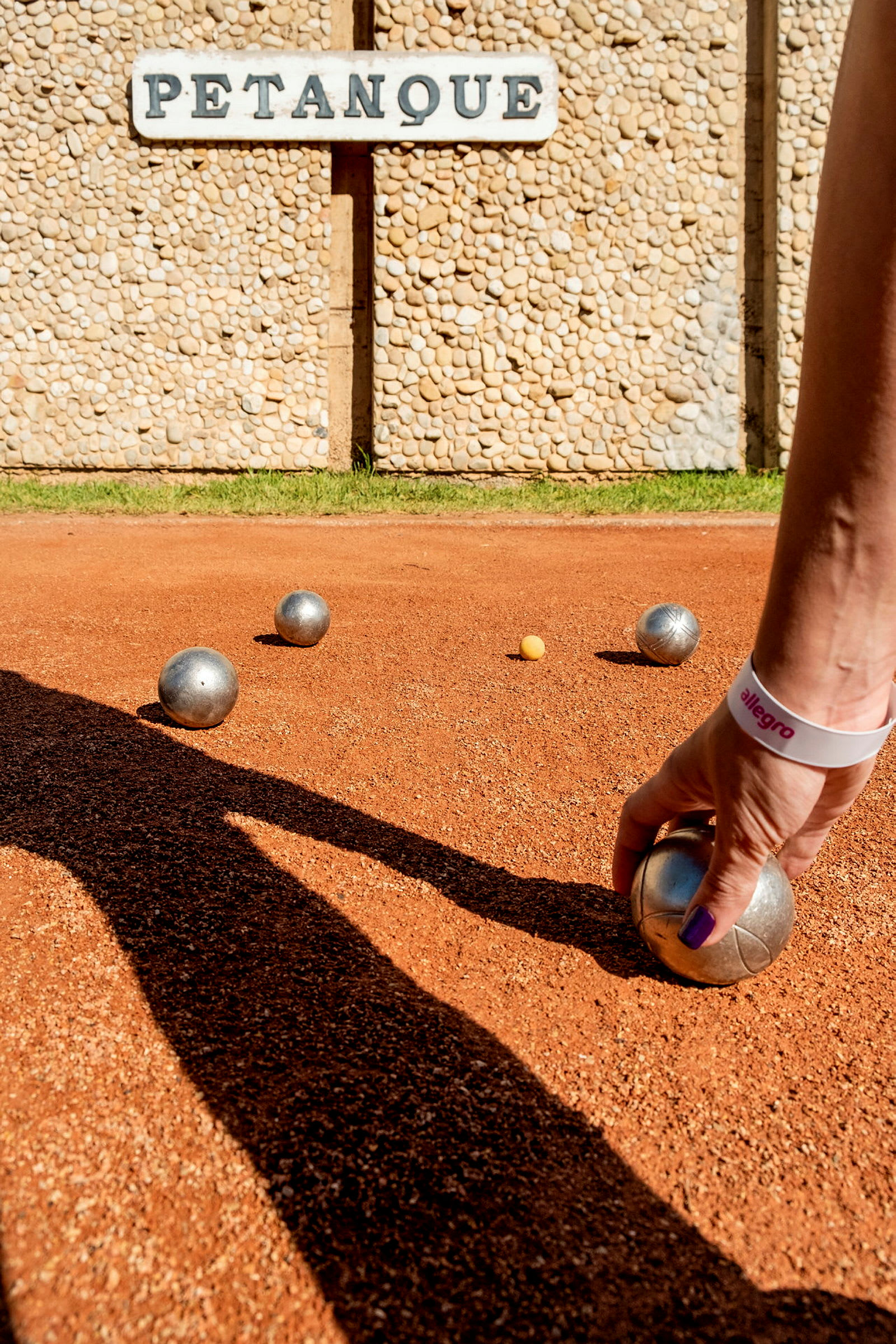 En hand håller en metallboll på en petanquebana. (AI-genererad text)