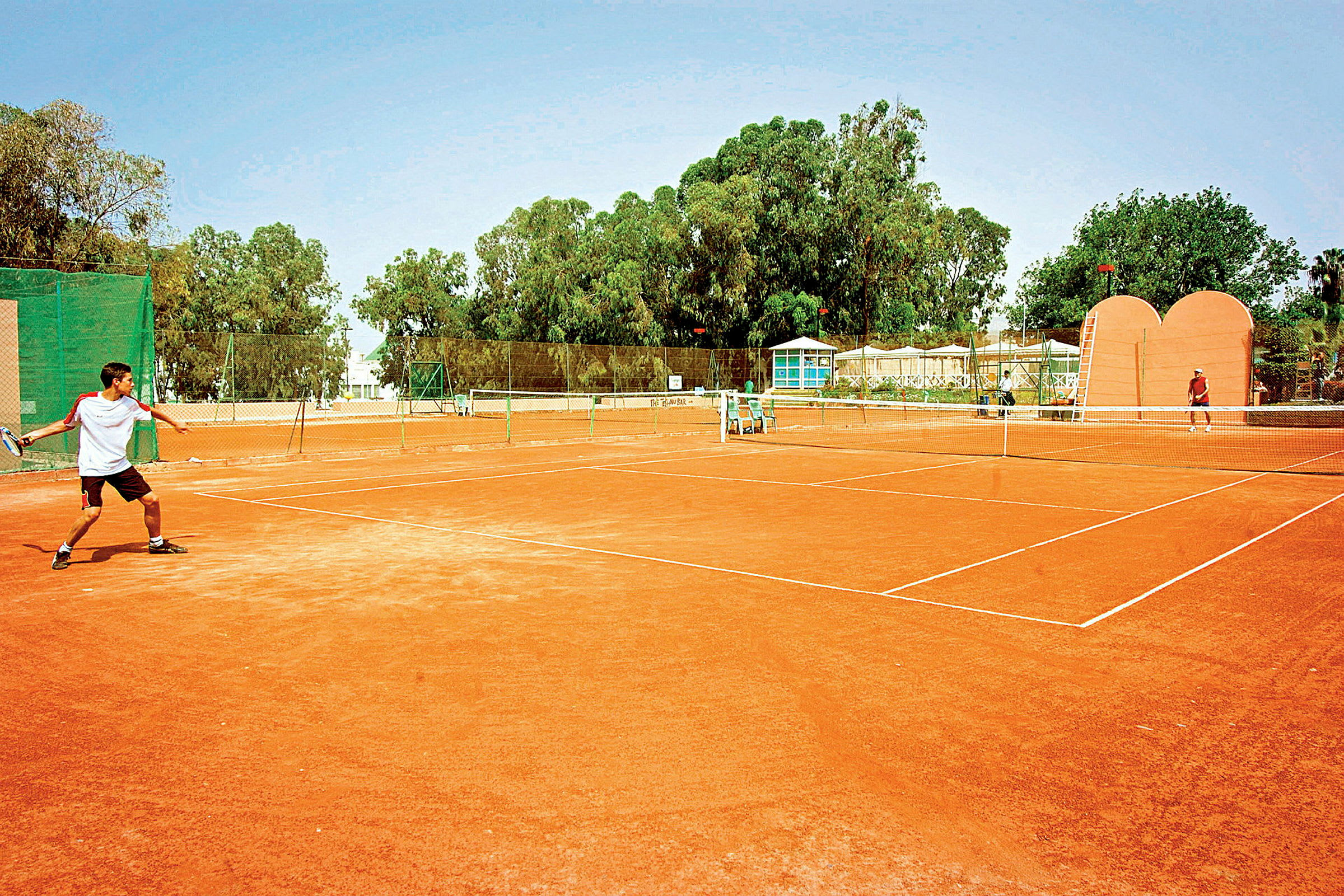 En tennisplan utomhus med två personer som spelar tennis. (AI-genererad text)