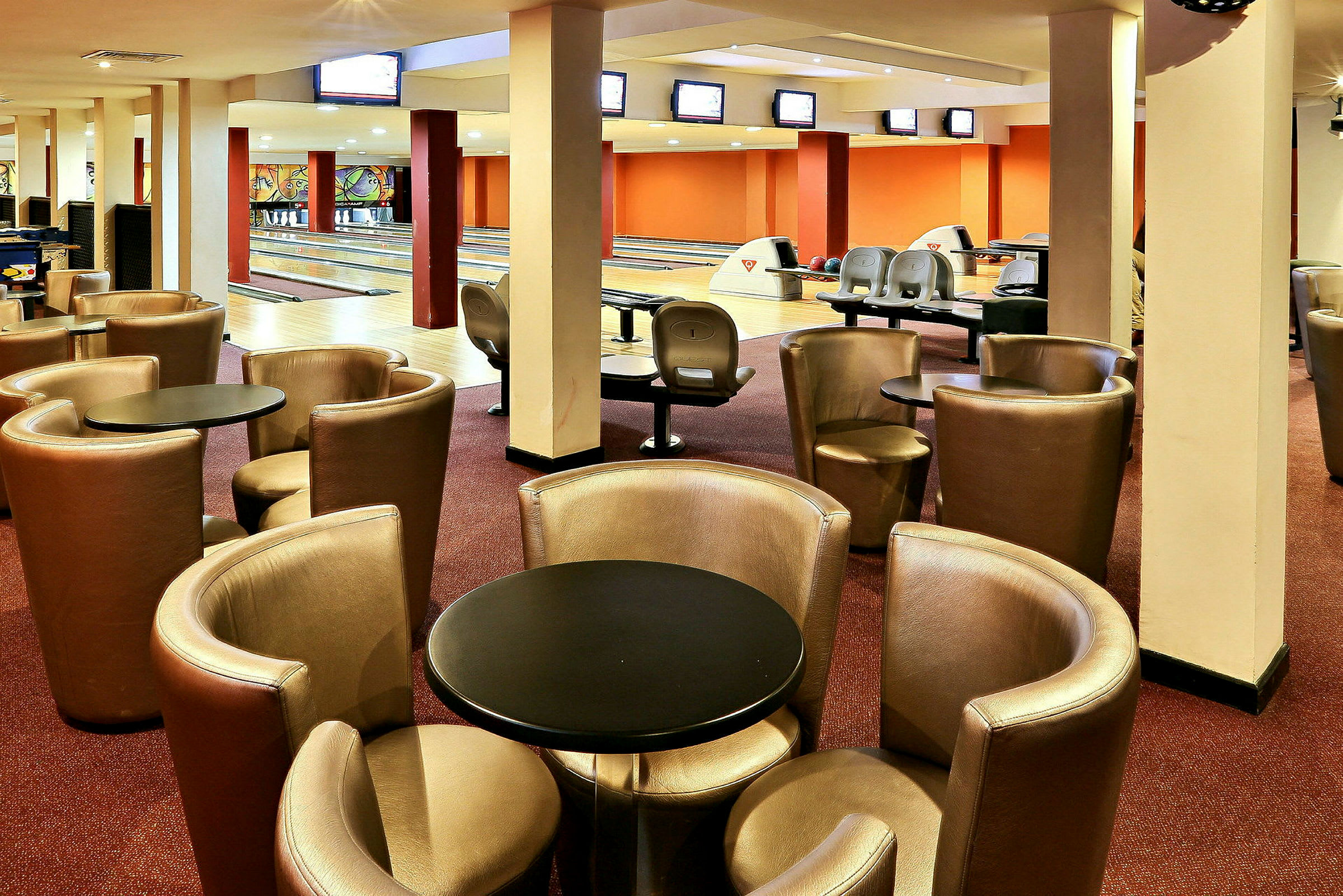 Ett bowlingområde med flera banor i bakgrunden och fåtöljer och bord i förgrunden. (AI-genererad text)