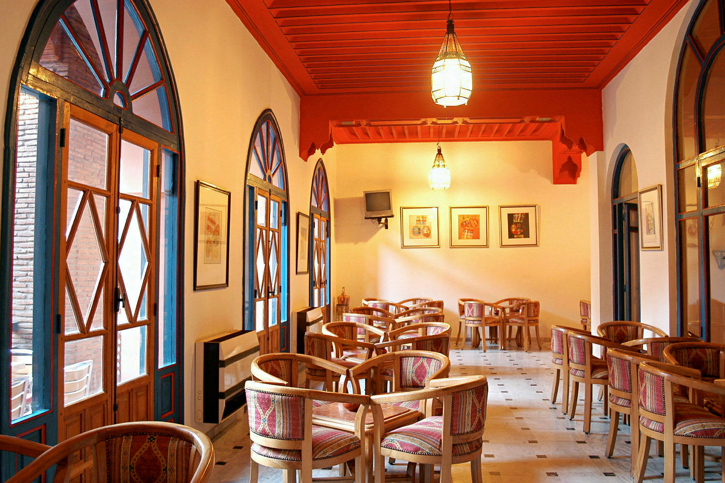 Interiörbild av ett kafé eller restaurang med trästolar och bord, färgglada textilier och bågformade fönster. (AI-genererad text)
