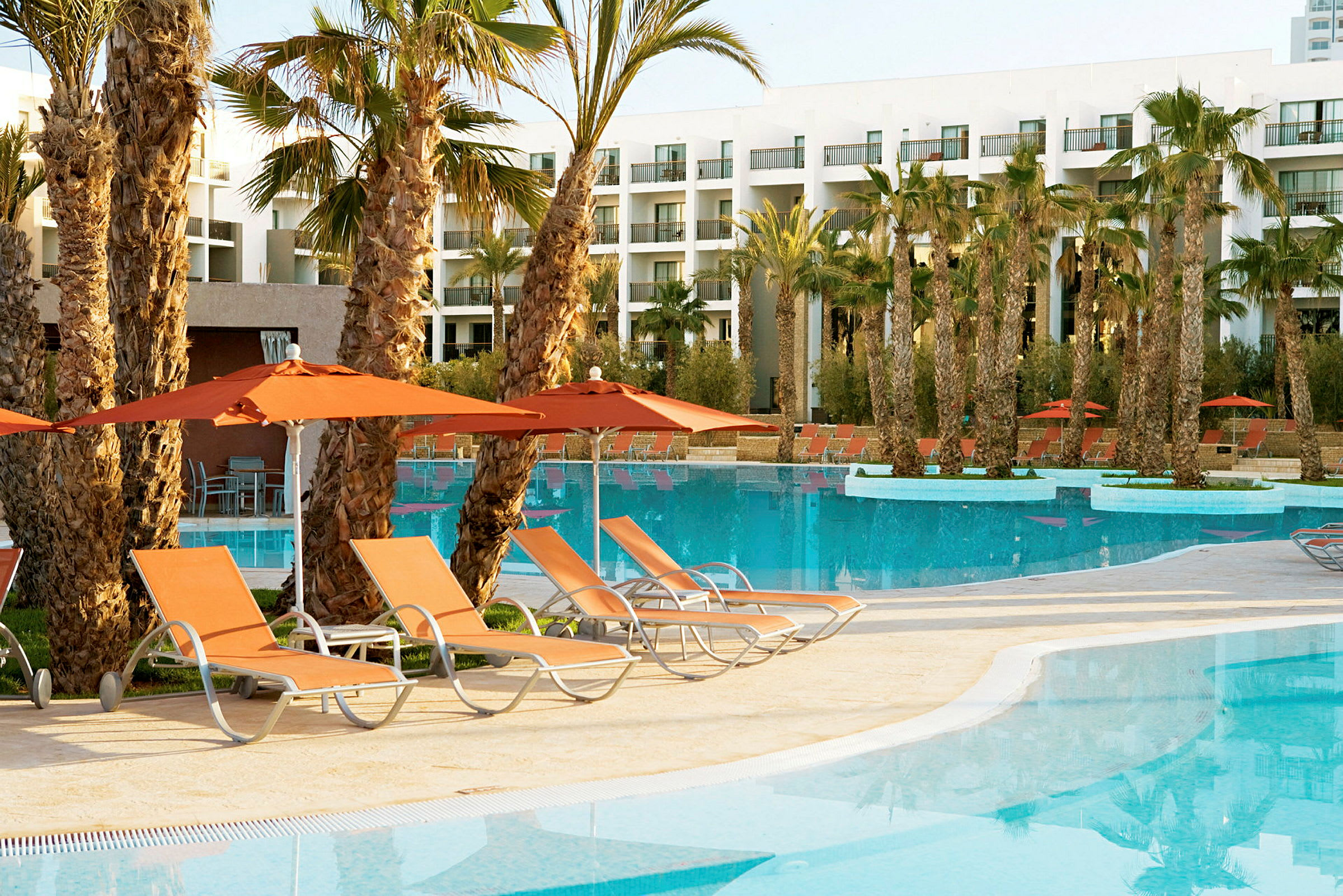 Poolområde vid ett hotell med solstolar och parasoller vid vattnet. (AI-genererad text)