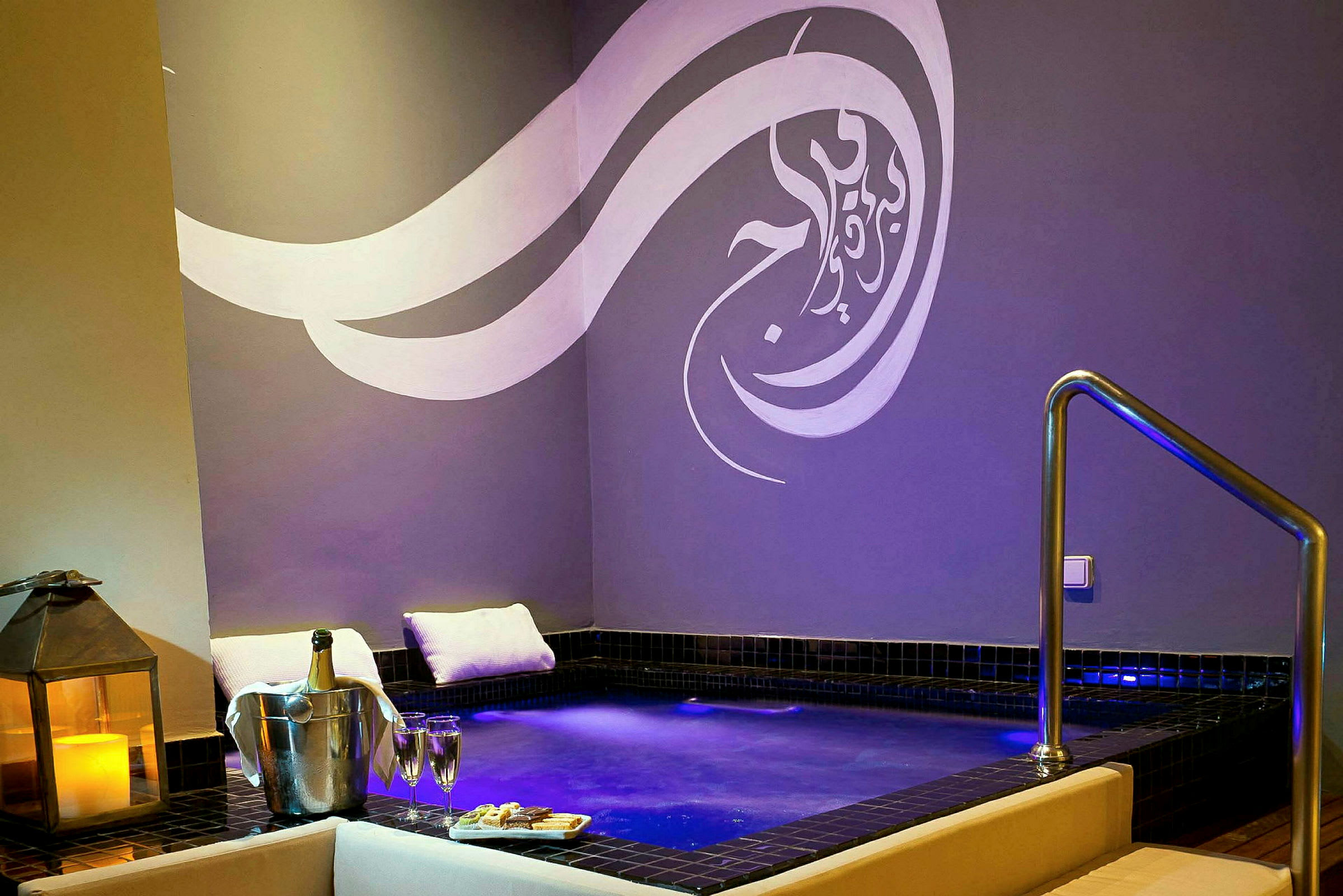 Ett spaområde med en mindre pool omgiven av kuddar, stearinljus och champagne. (AI-genererad text)