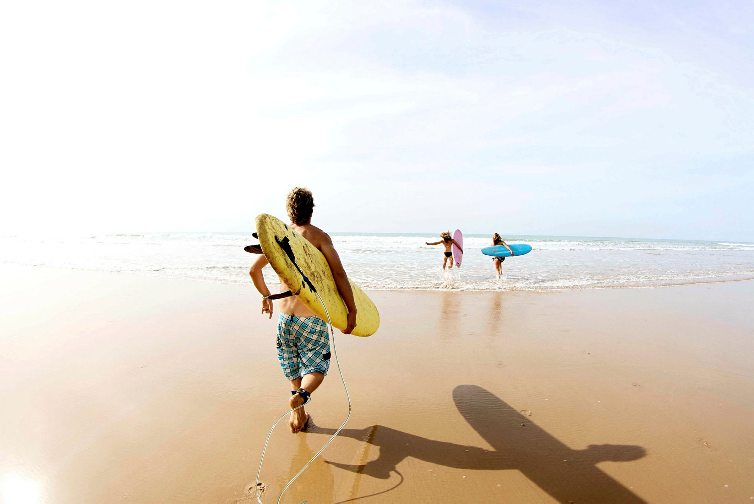 En grupp människor med surfbrädor går ut i havet på en strand. (AI-genererad text)