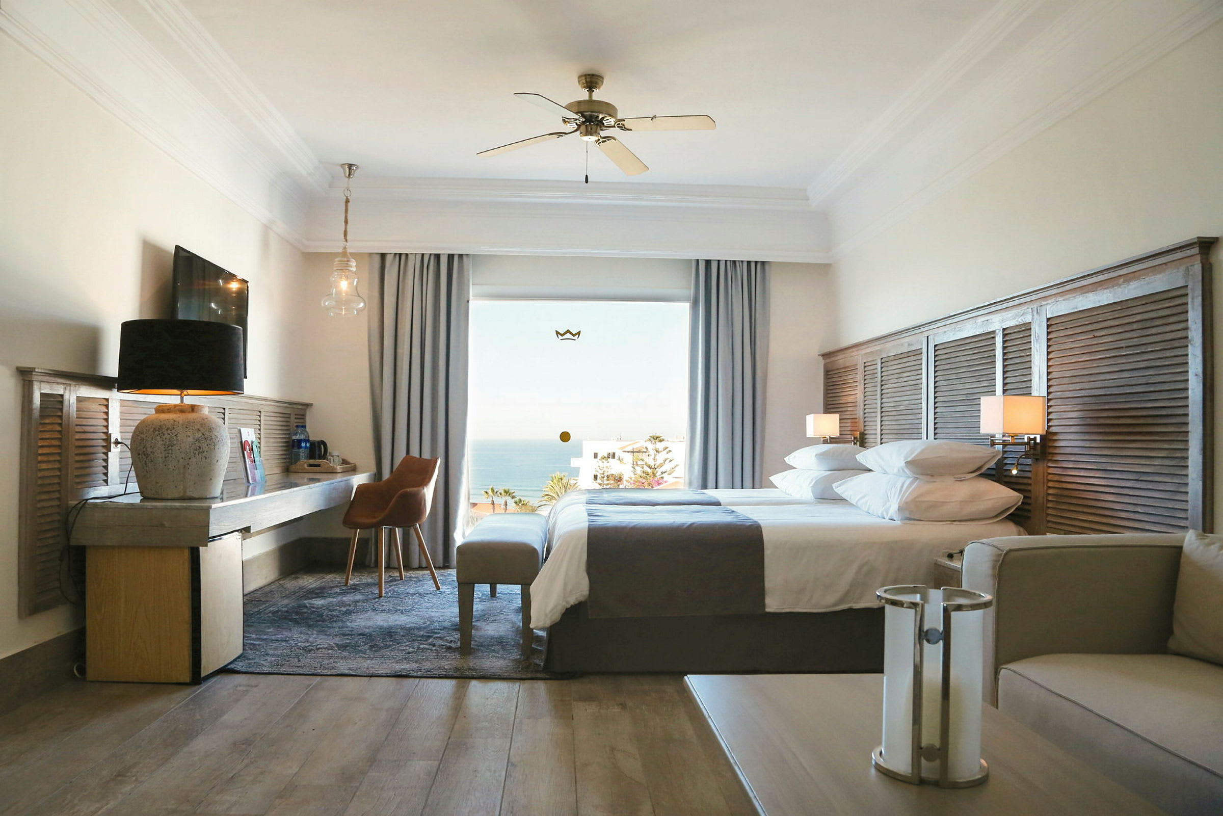 Ett hotellrum med två sängar, en sittgrupp och utsikt över havet genom fönstret. (AI-genererad text)