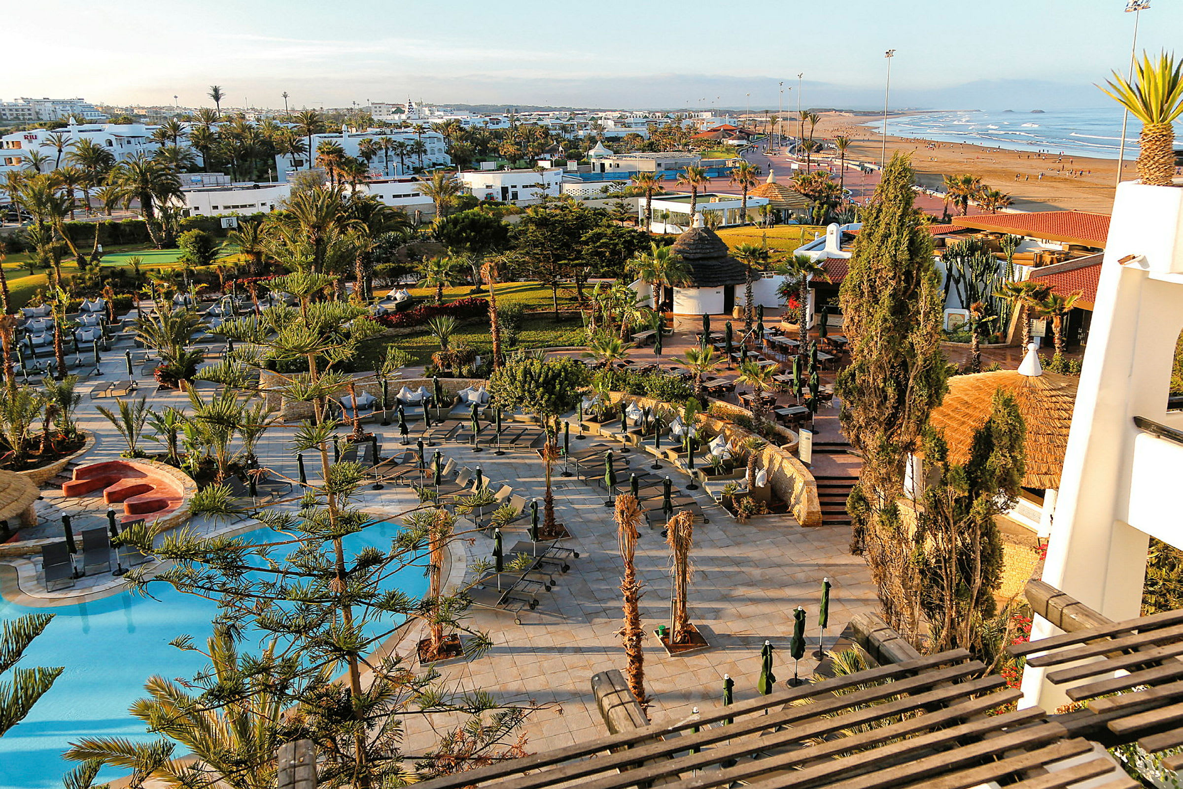 Ett hotellområde med pool, solstolar och omgivande trädgårdar nära en strand. (AI-genererad text)