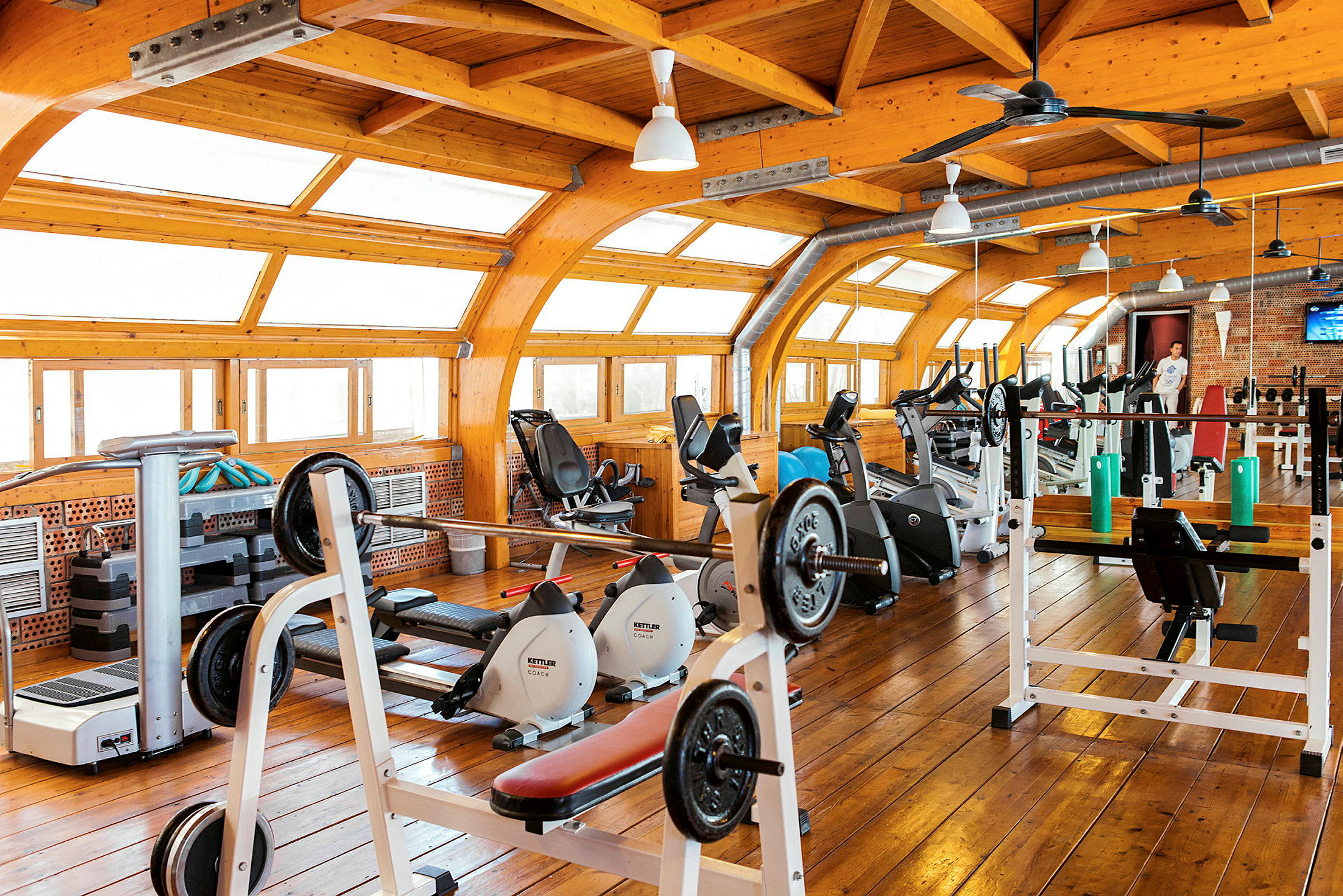 Ett ljust gym med träningsutrustning, stort fönsterparti och trädetaljer. (AI-genererad text)