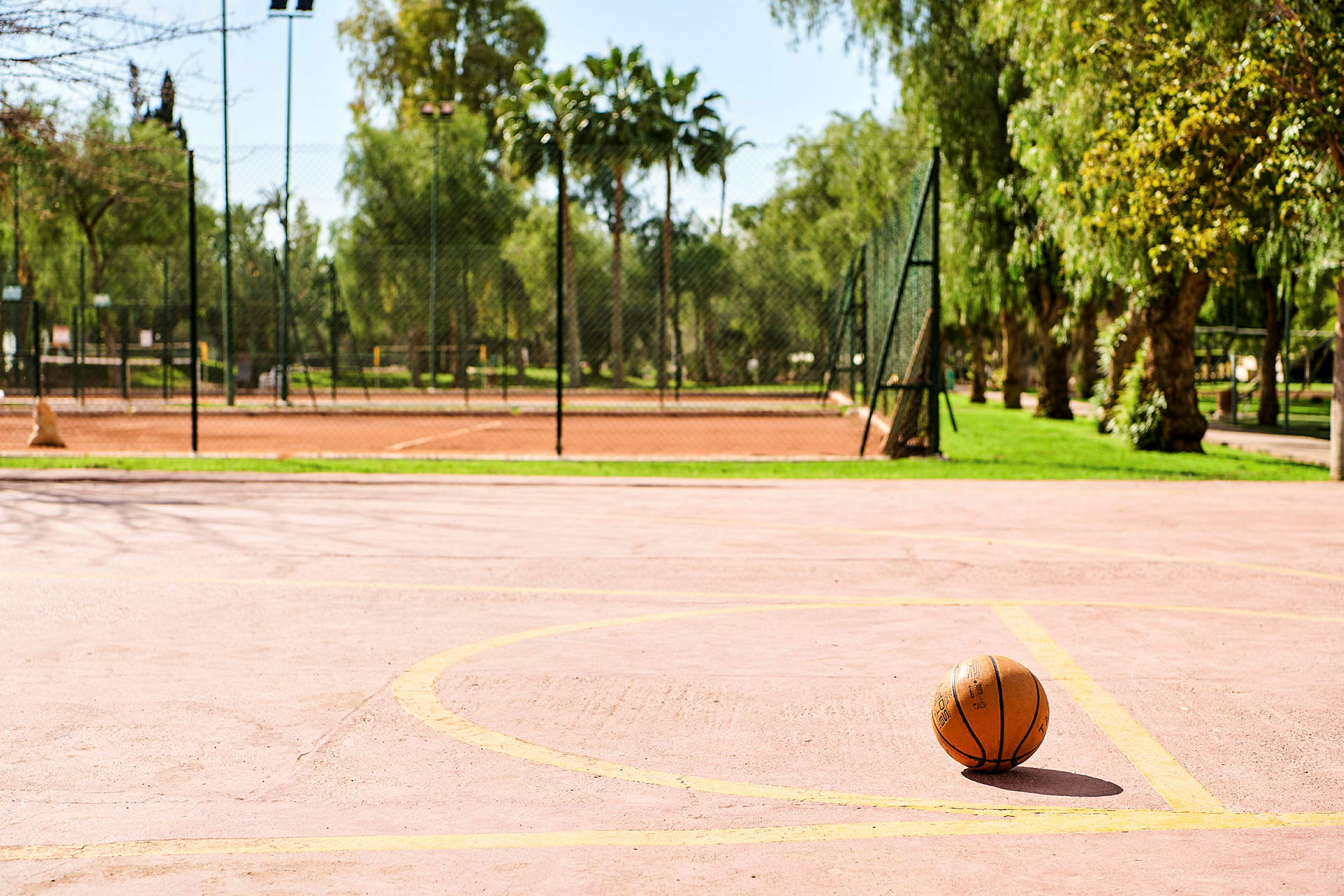 En basketboll på en tom basketplan med träd och stängsel i bakgrunden. (AI-genererad text)