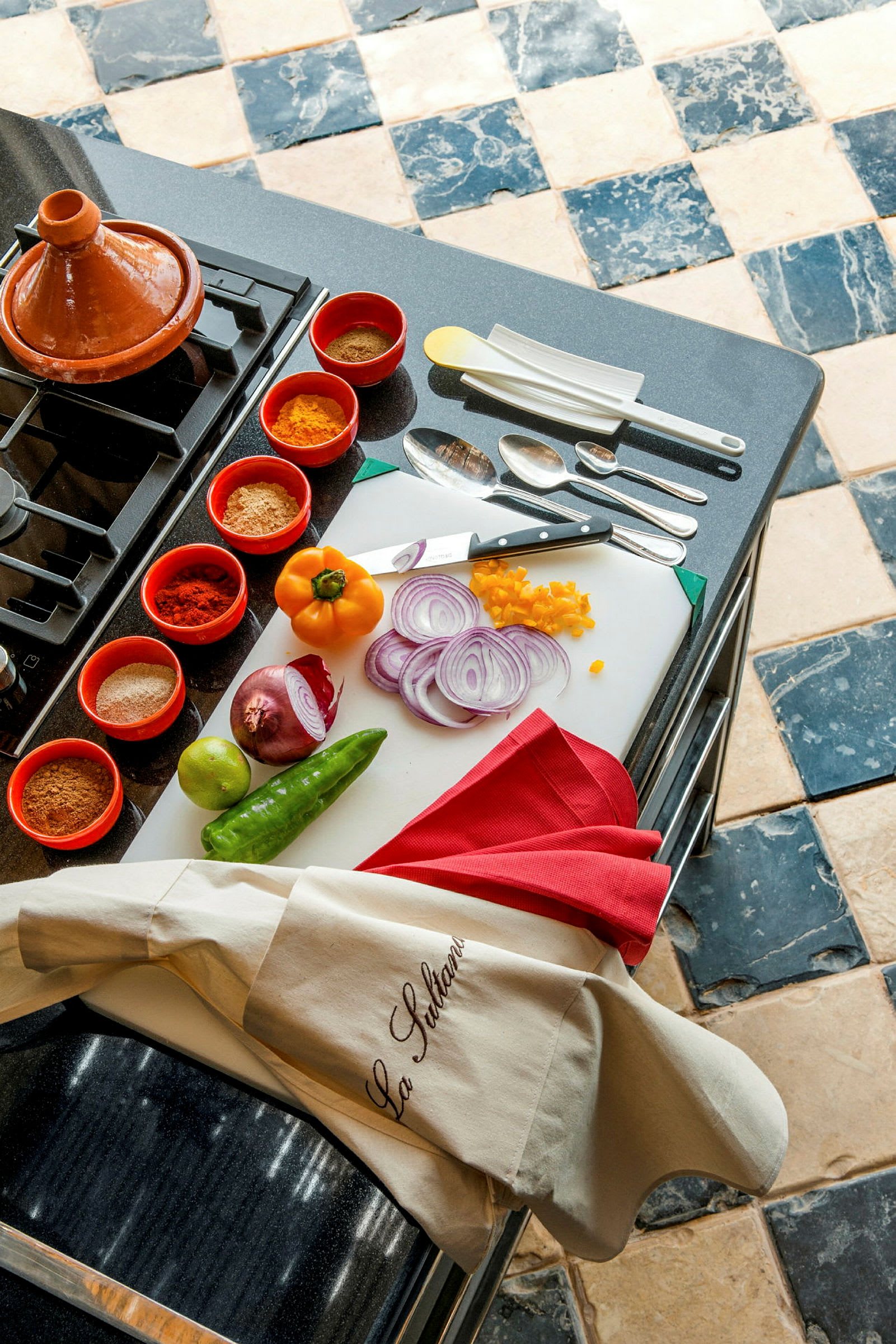 Ett köksbord med ingredienser inklusive grönsaker, kryddor och köksutrustning samt en taginegryta. (AI-genererad text)