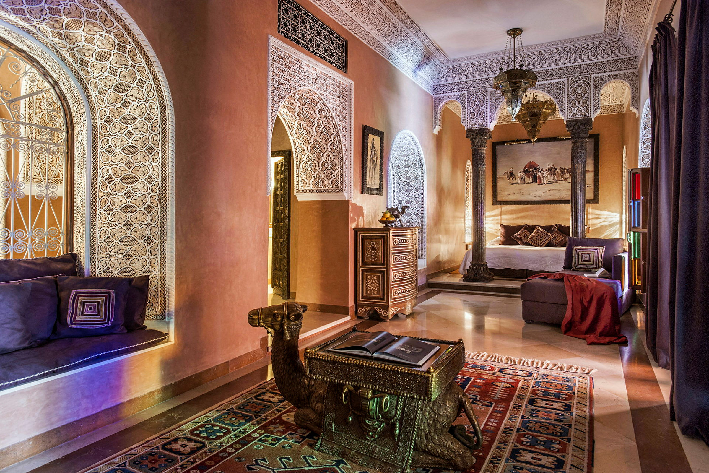 Ett elegant inrett rum med dekorativa gipsmönster, arkitektoniska bågar, orientaliska möbler och varm belysning. Ett bord formad som en kamel står på en färgglad matta. (AI-genererad text)