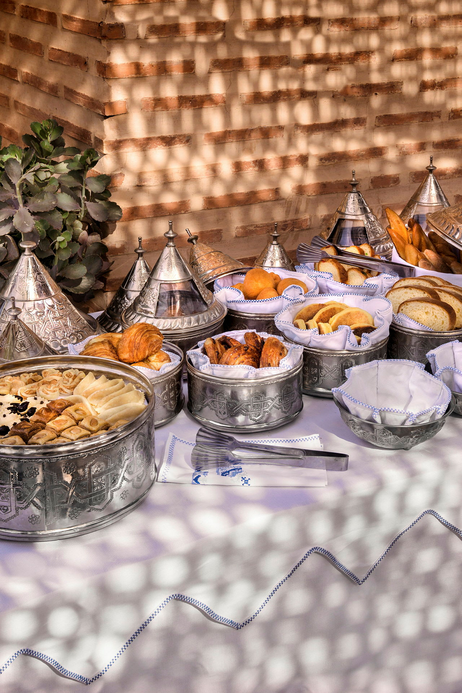 En buffé med bakverk och bröd i dekorativa metallfat på ett dukat bord. (AI-genererad text)