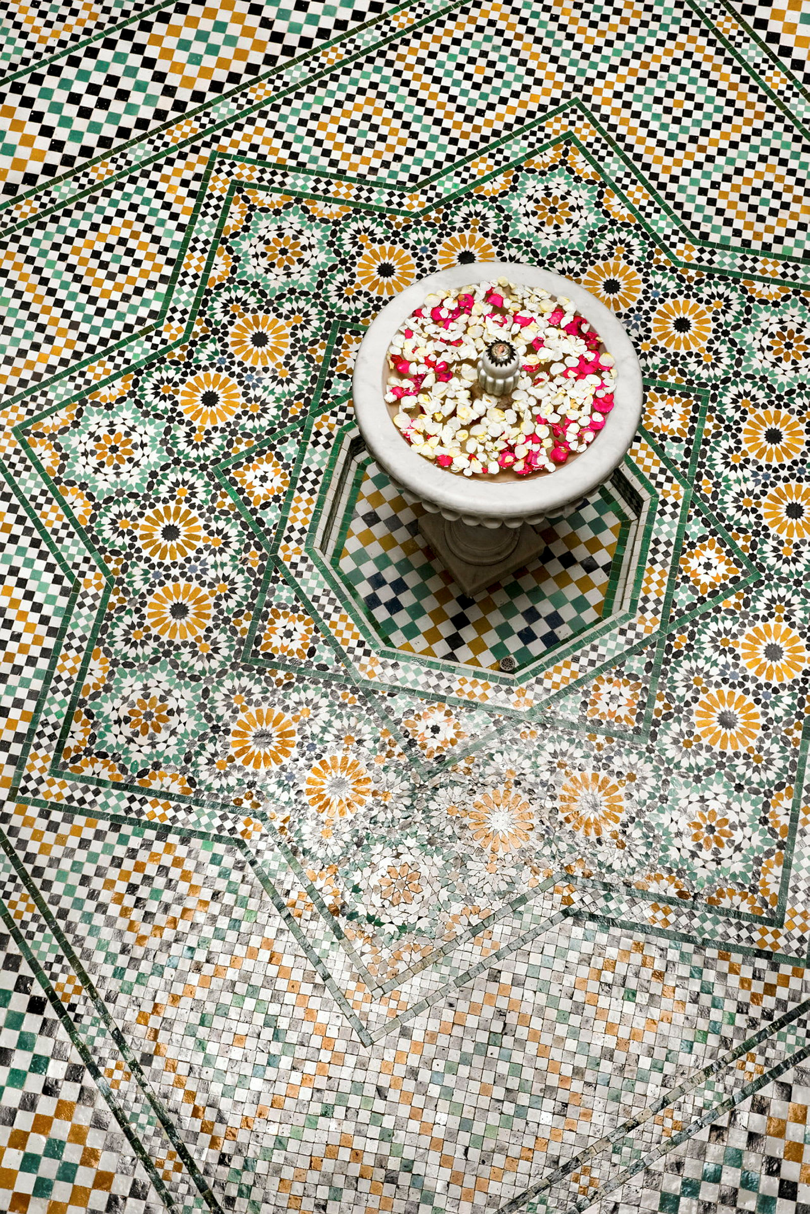 En mönstrad mosaikgolv med en dekorativ fontän fylld med vatten och blomblad. (AI-genererad text)