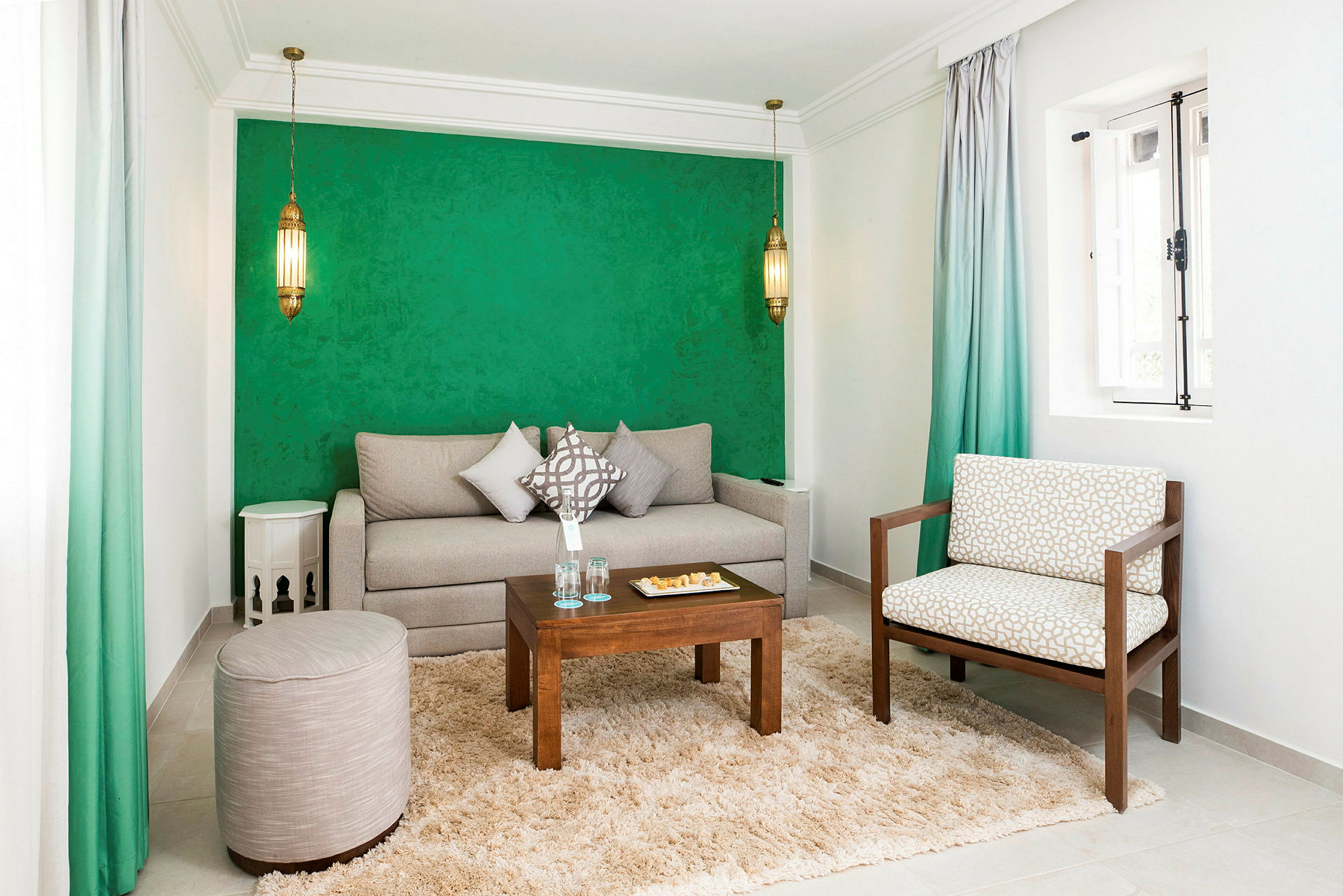 Ett vardagsrum med grön vägg, en beige soffa, en stol, en liten träbord och en matta. (AI-genererad text)