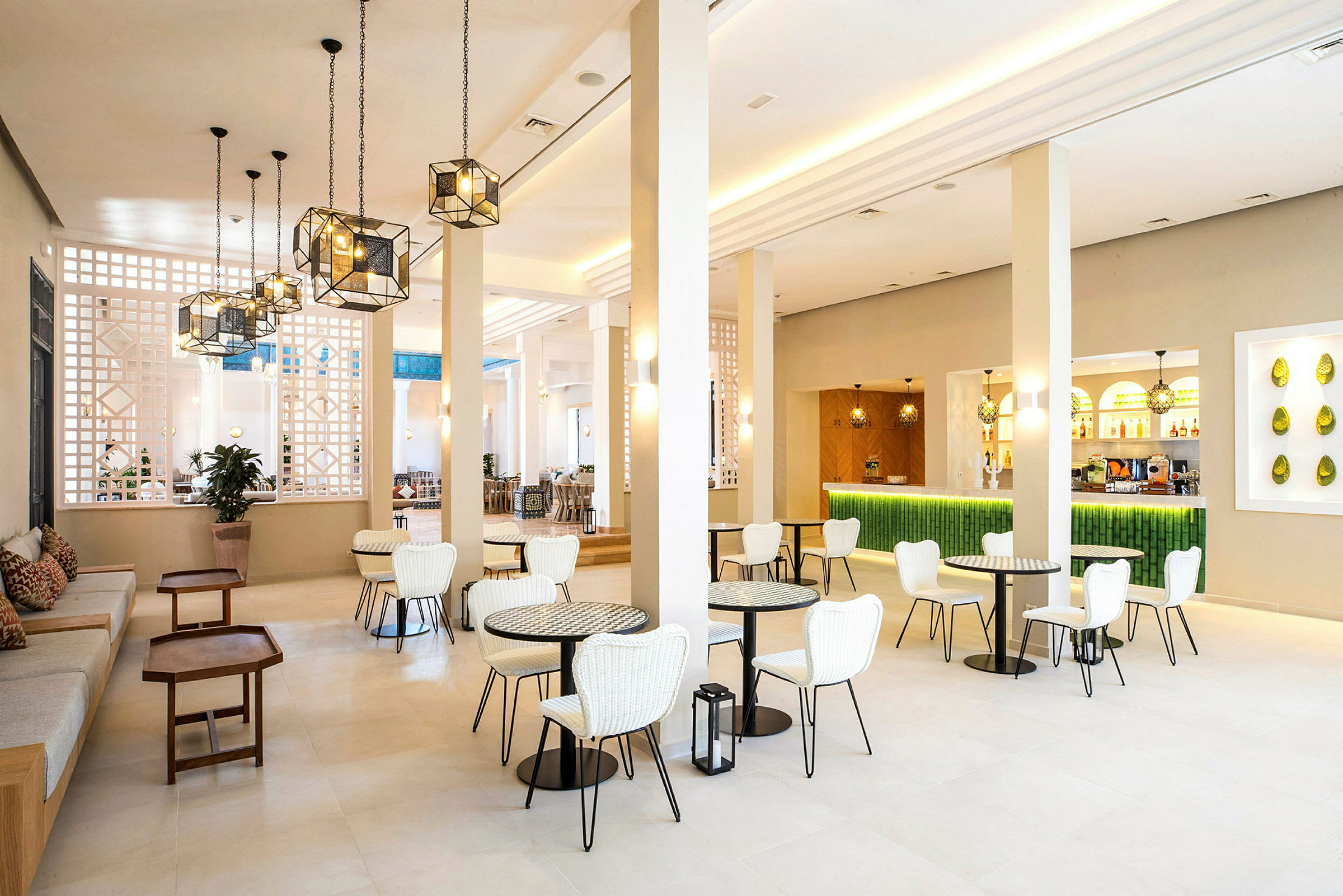 En ljus och modern lounge med vita stolar, små bord och en grön bardisk. (AI-genererad text)