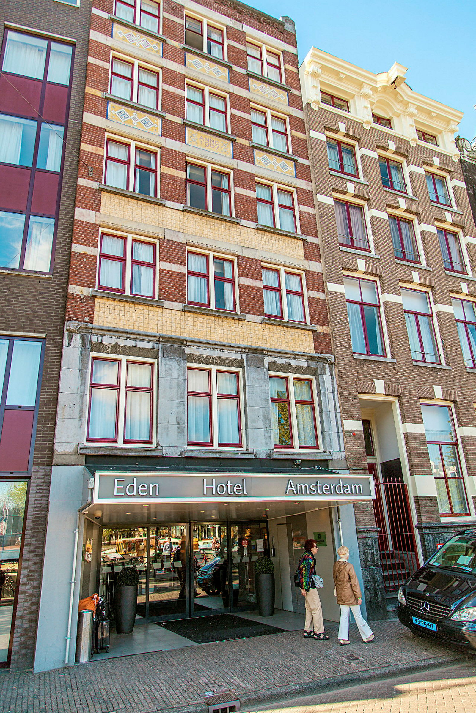 Framsidan av Eden Hotel Amsterdam med ingång och personer framför byggnaden. (AI-genererad text)