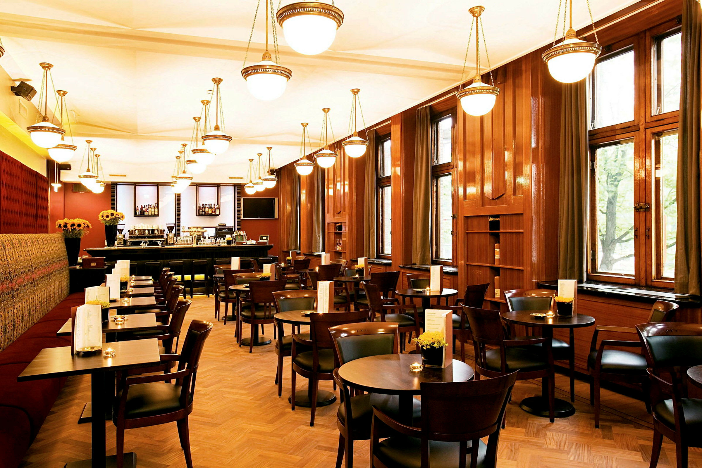 Bild av ett restauranginteriör med träbord och stolar, stora fönster och hängande lampor i taket. (AI-genererad text)