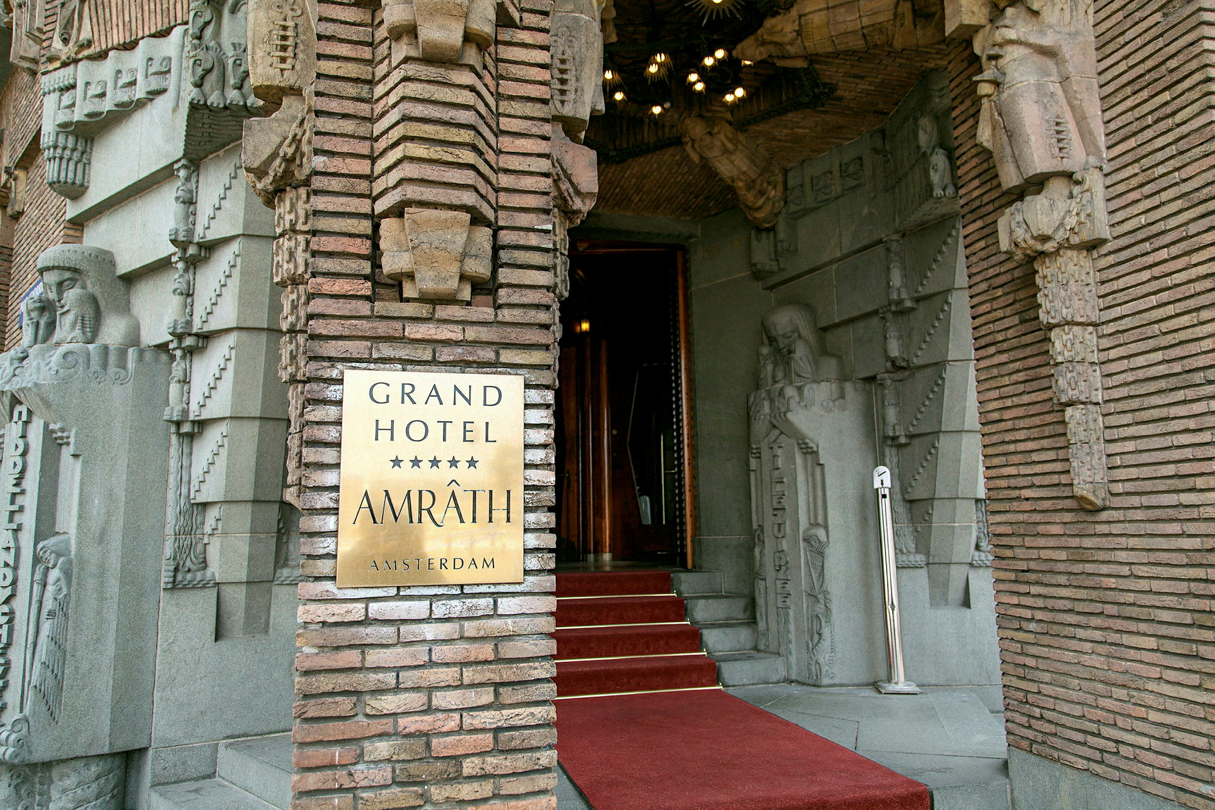 Entrédörr till Grand Hotel Amrâth Amsterdam med dekorativa stenutsmyckningar. (AI-genererad text)