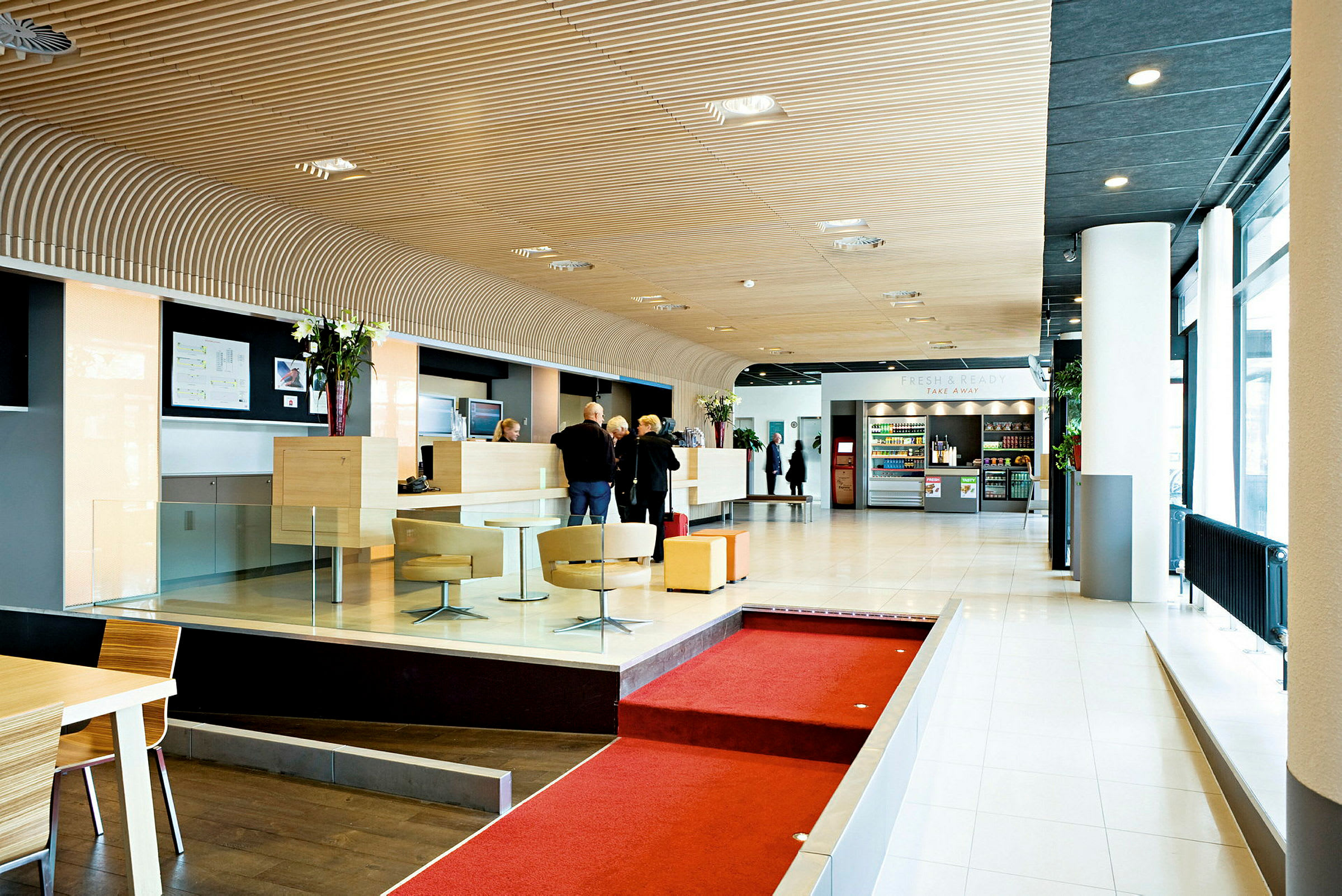 Ljus och modern hotellobby med reception, sittgrupper och en kiosk med drycker och snacks. (AI-genererad text)