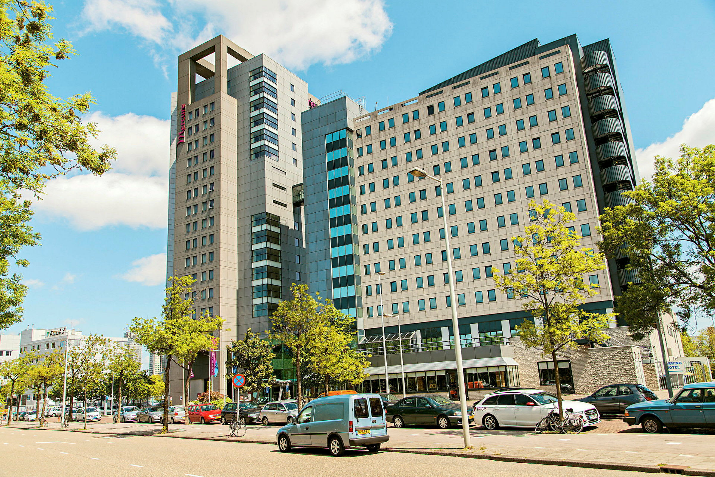 En modern byggnad med flera våningar omgiven av parkerade bilar och träd. (AI-genererad text)