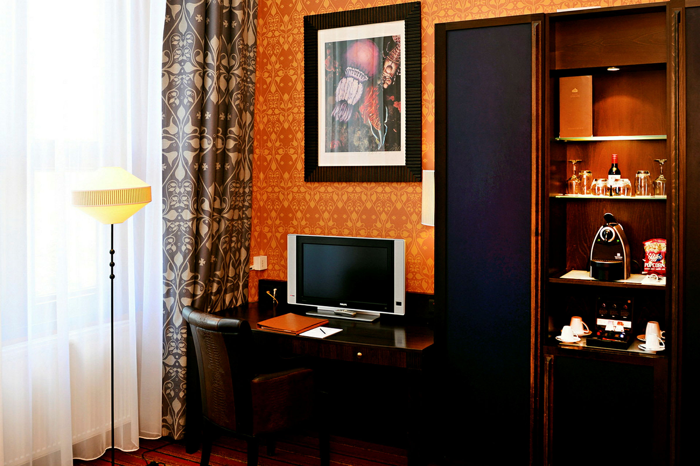 Ett hotellrum med skrivbord, stol, tv, bordslampa och ett skåp med drycker och kaffemaskin. (AI-genererad text)
