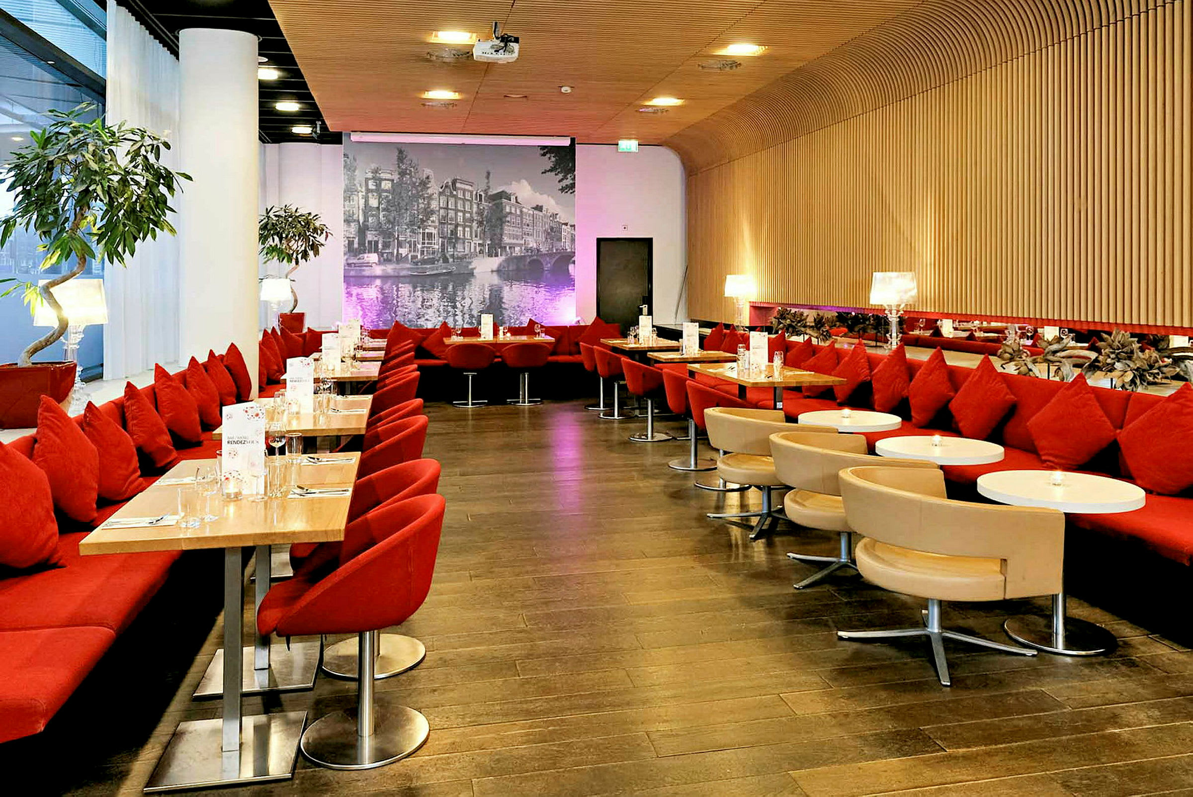 Atmosfärisk restaurang med röda sittplatser, små bord och en fondvägg av en svartvit stadsbild. (AI-genererad text)