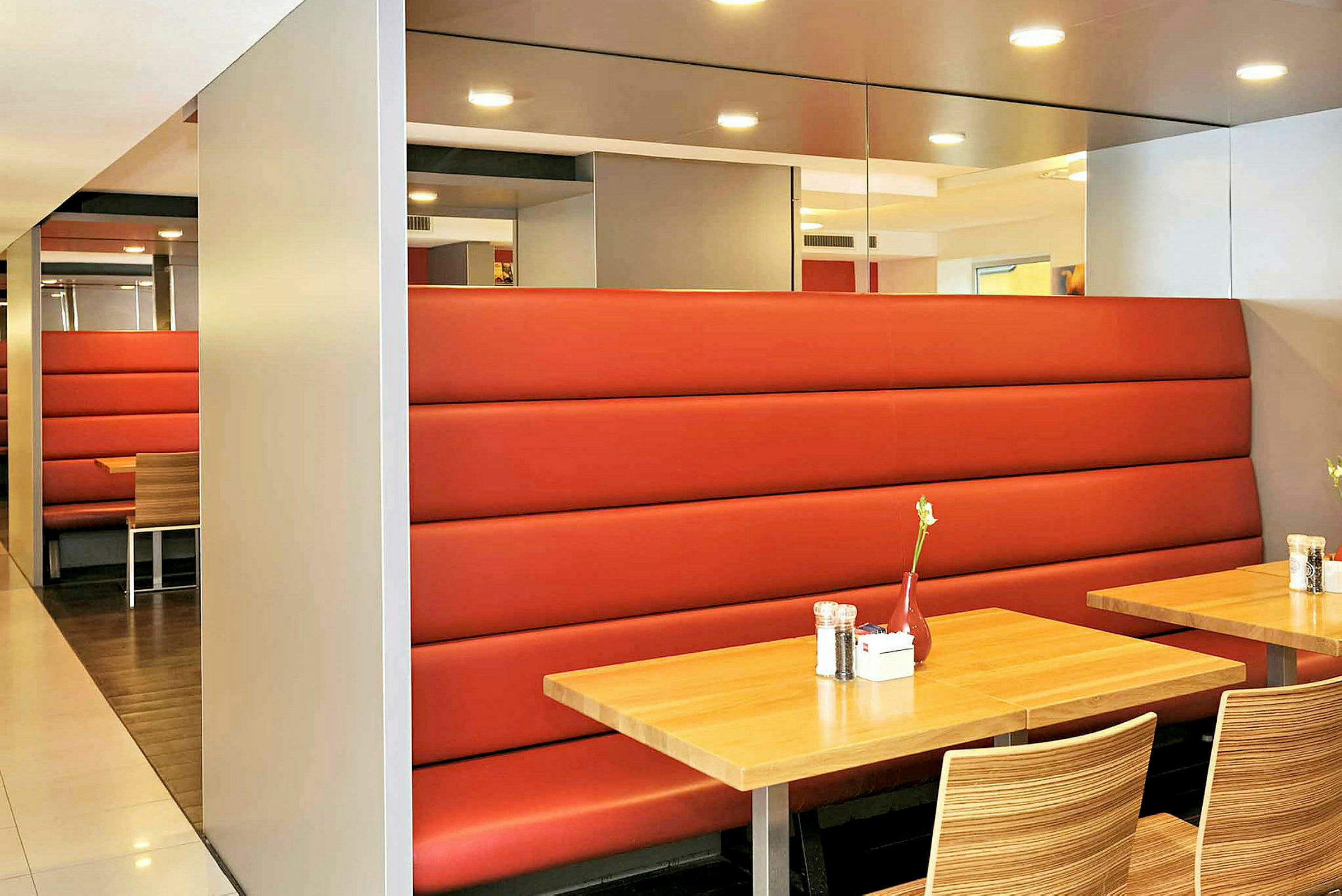 En interiör av en restaurang med träbord, röda soffor och stolar med trämönster. (AI-genererad text)