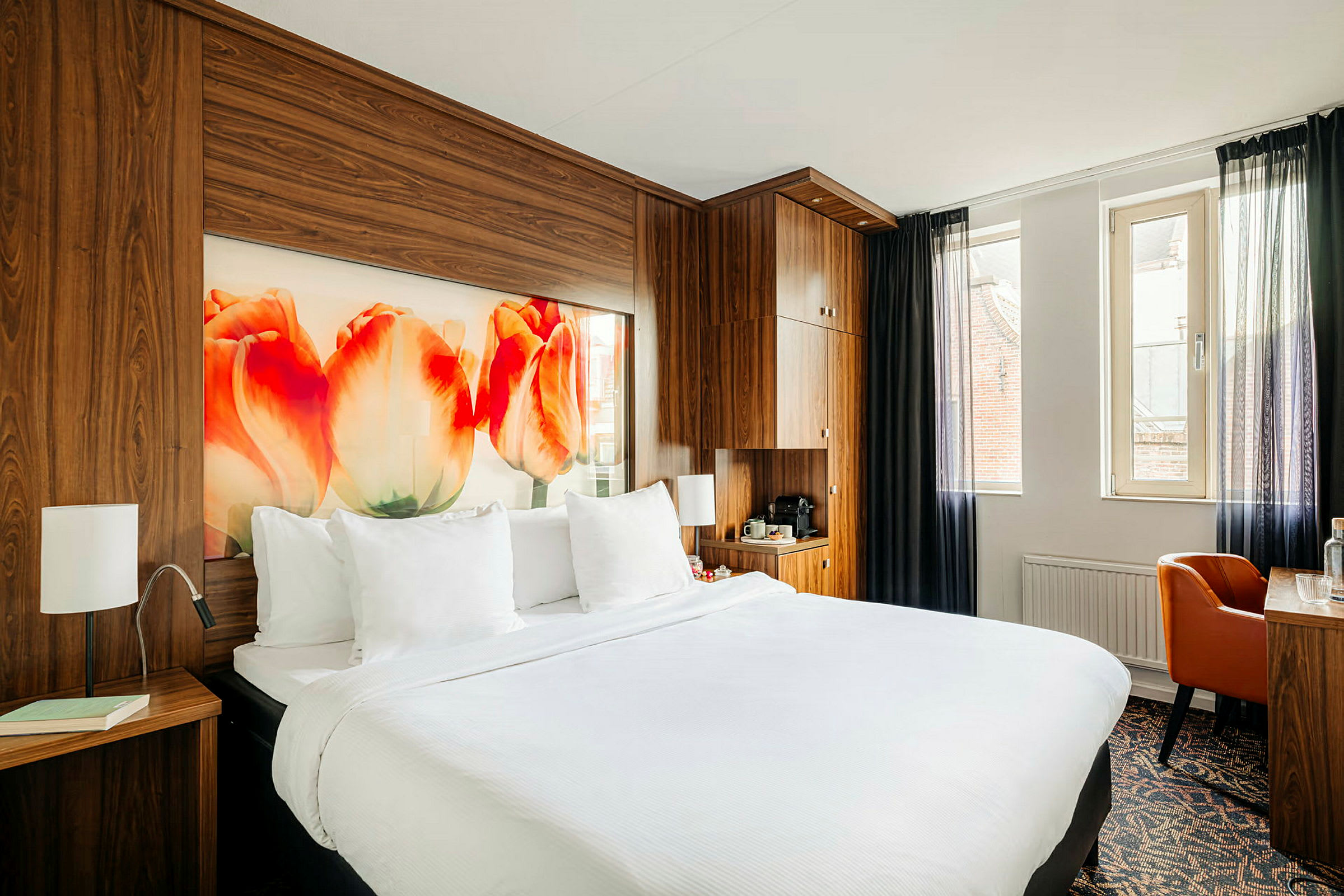 Hotellrum med en dubbelsäng, träpaneler, tulpanmotiv på väggen och ett skrivbord vid fönstret. (AI-genererad text)