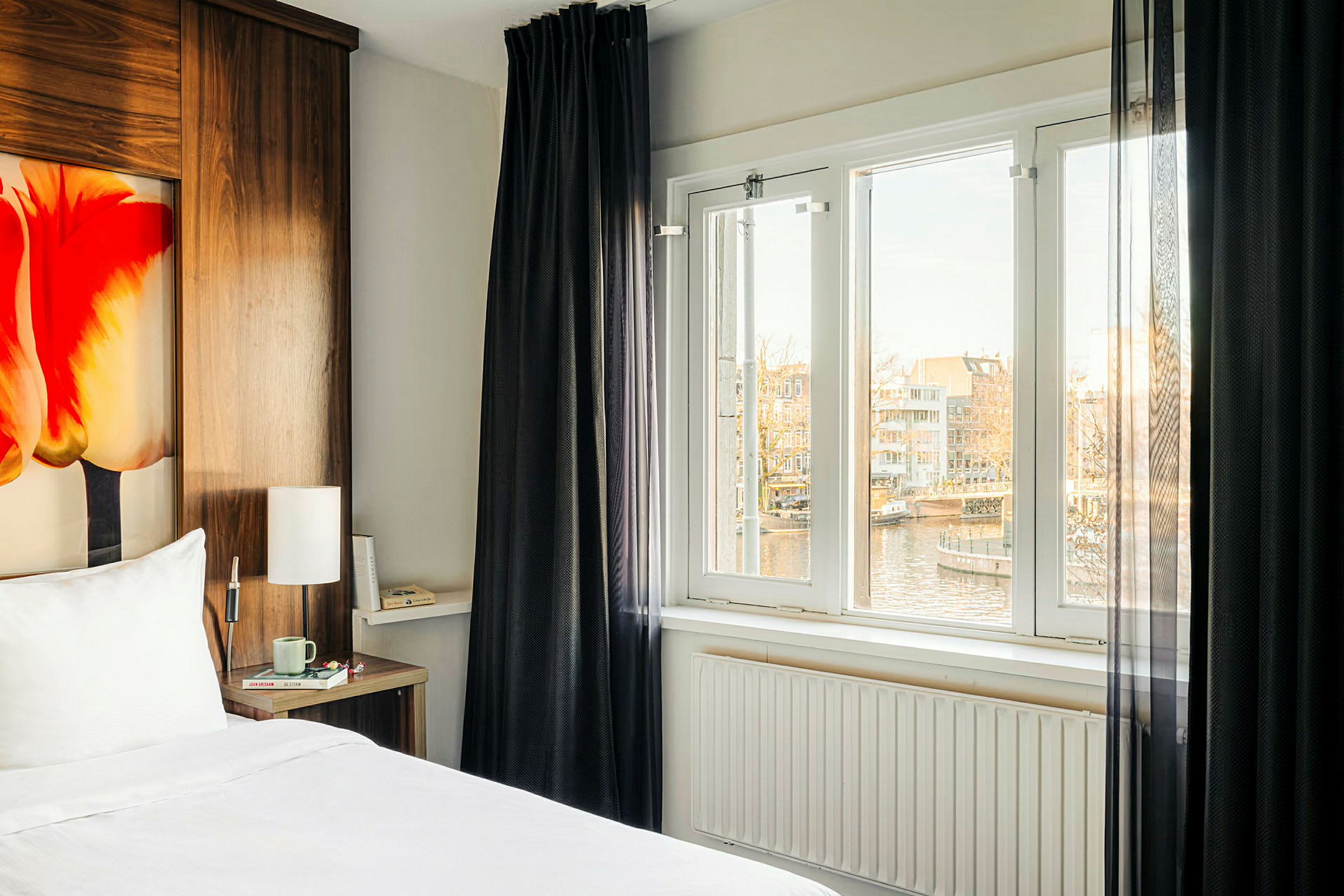 Ett hotellrum med en säng, ett fönster med utsikt över en kanal och hus. (AI-genererad text)