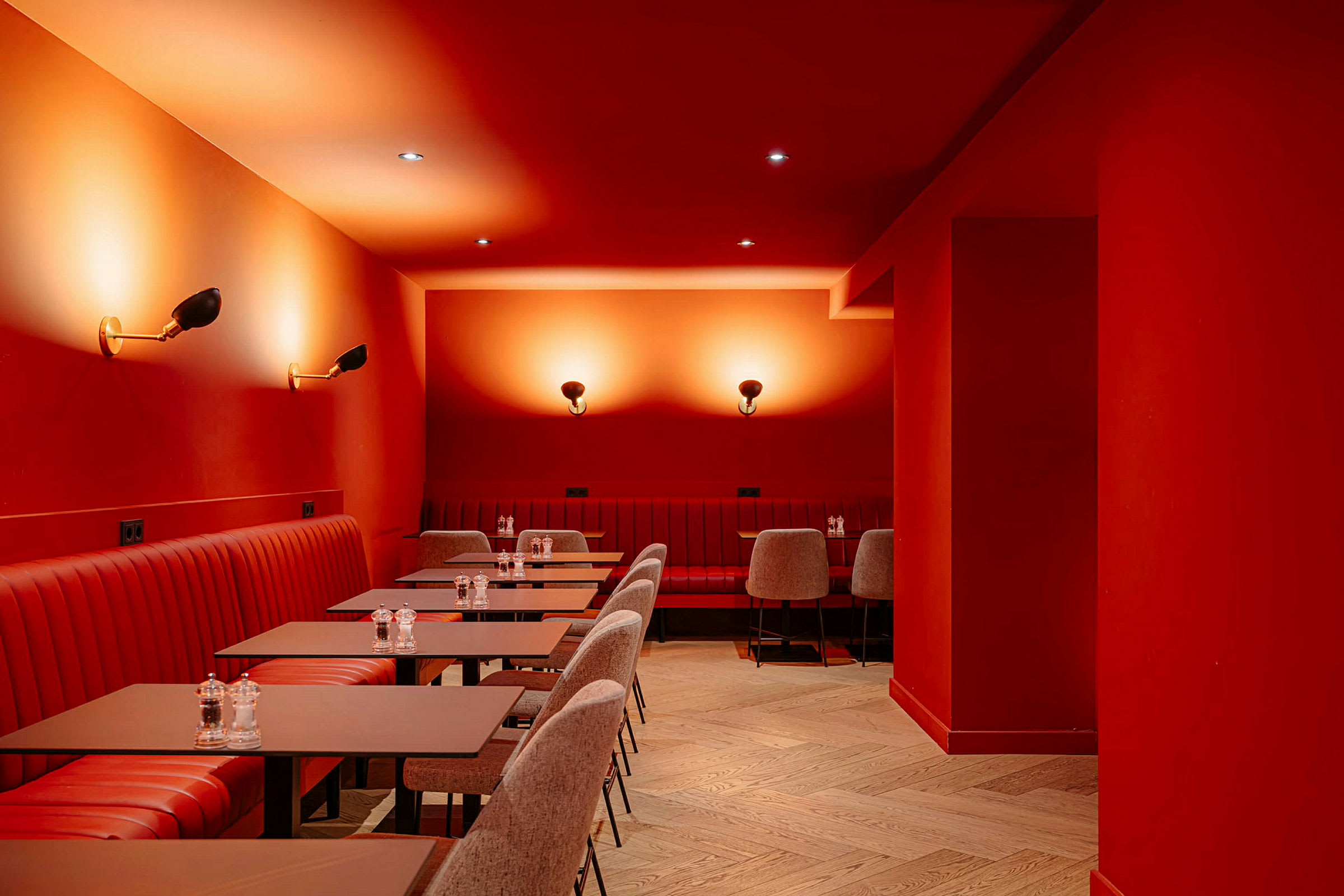 Bild på en interiör av en restaurang eller café med röda väggar och tak. Röd stoppning på sittplatserna och matchande bord. Belysning med vägglampor skapar en varm atmosfär. (AI-genererad text)