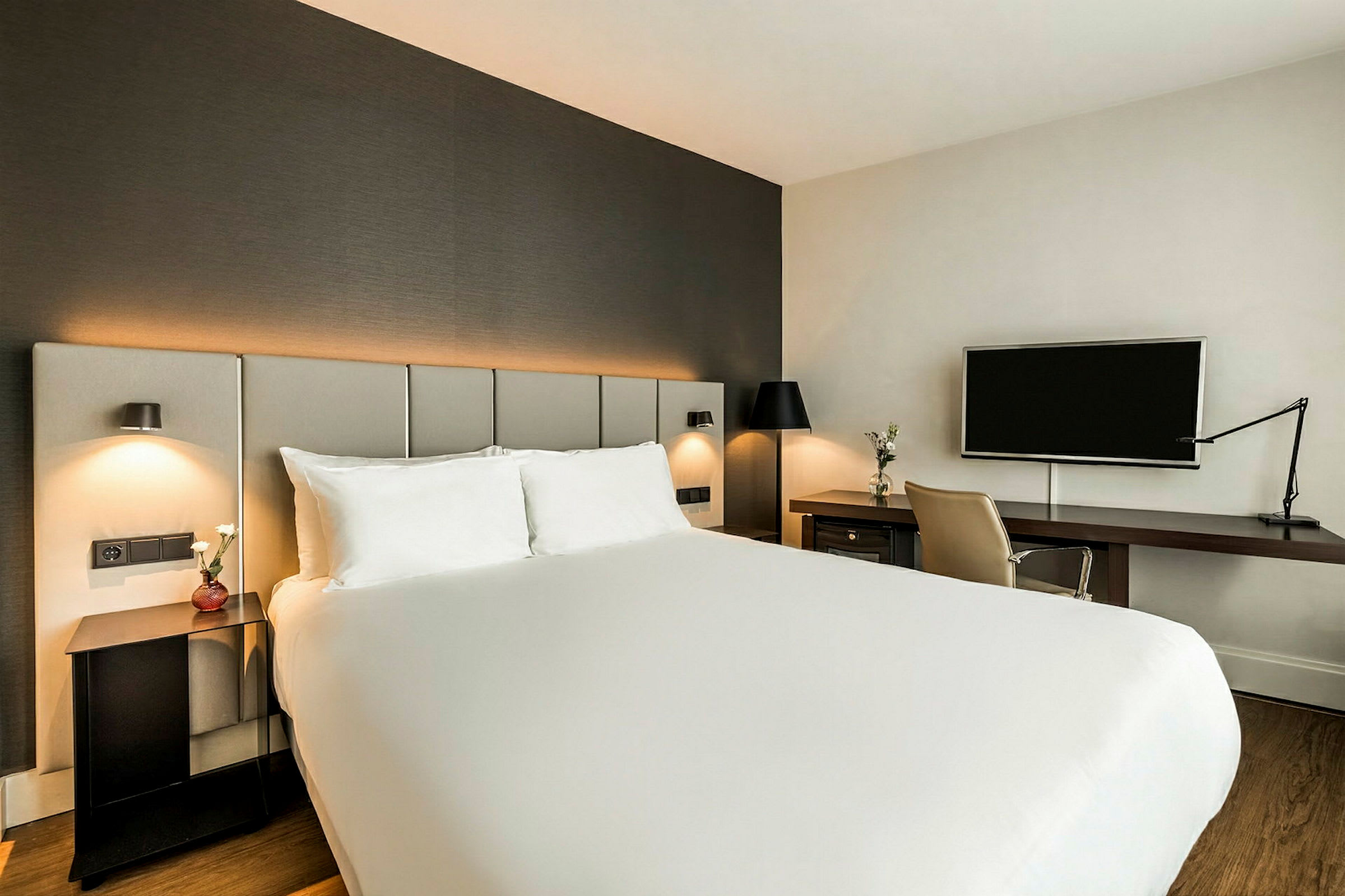 Ett hotellrum med en stor säng, skrivbord med stol och en väggmonterad TV. (AI-genererad text)