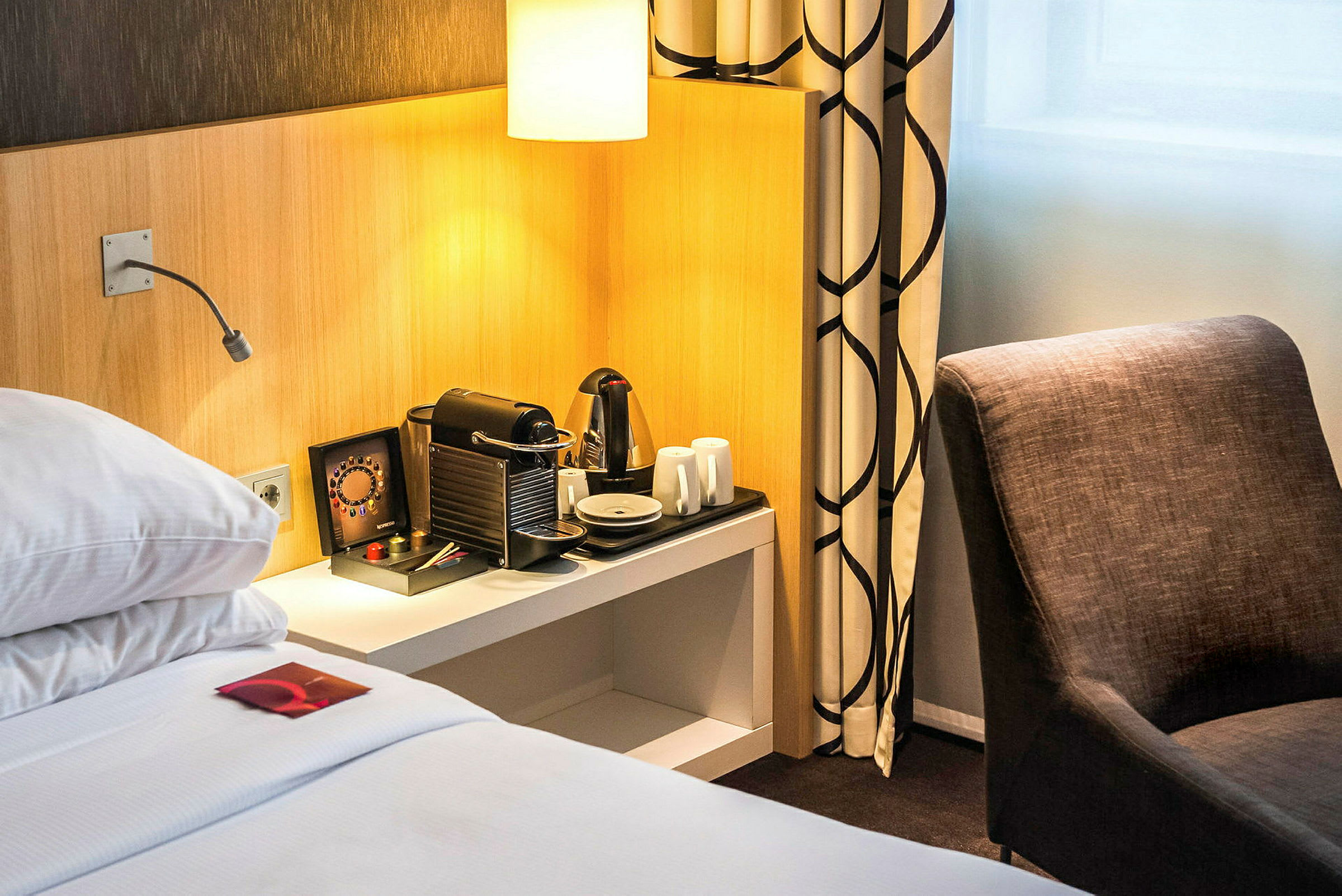 Hotellrum med säng, kaffemaskin och stol. (AI-genererad text)