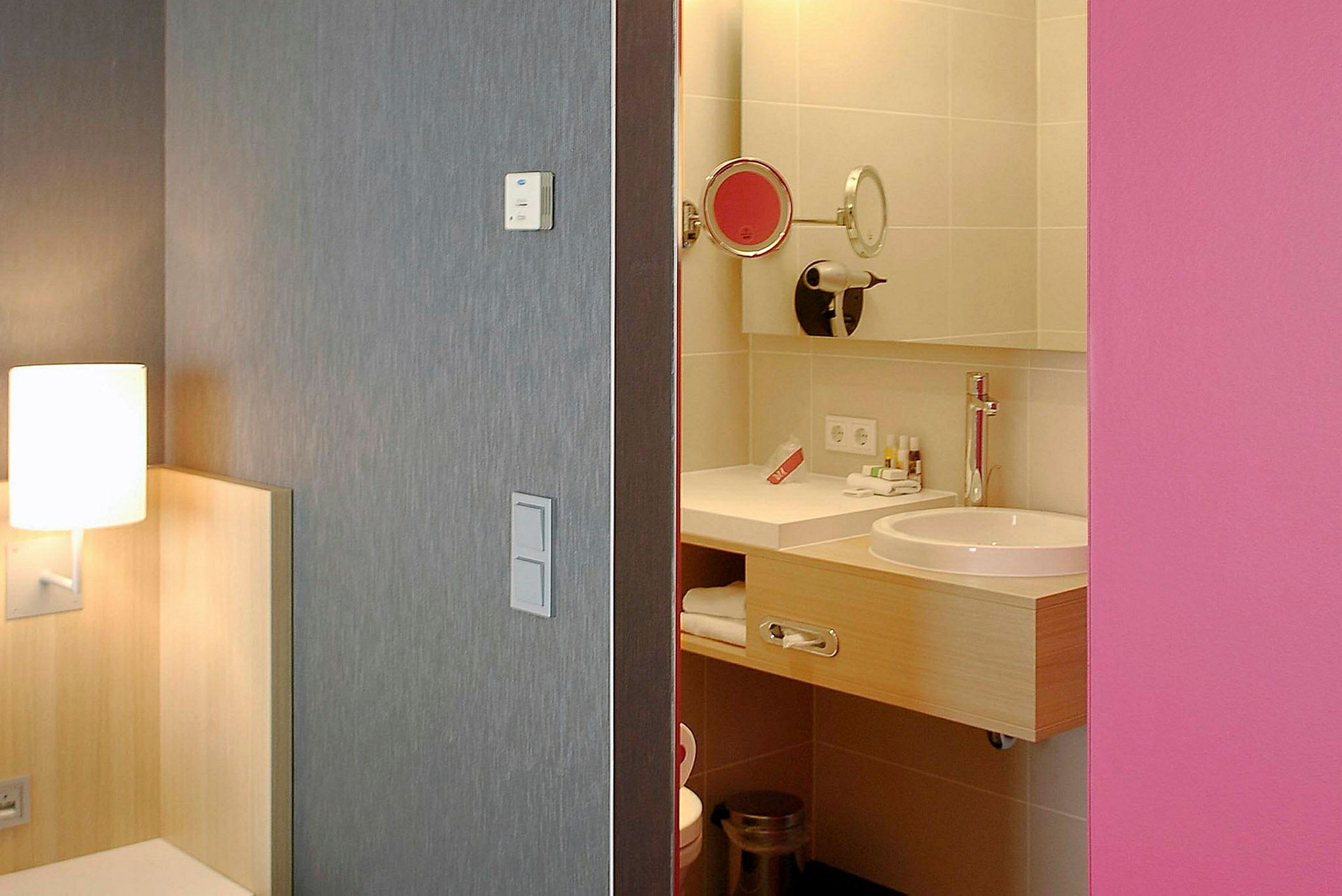 Hotellrum med en syn av badrummet, lampan och sängens hörn synliga. (AI-genererad text)