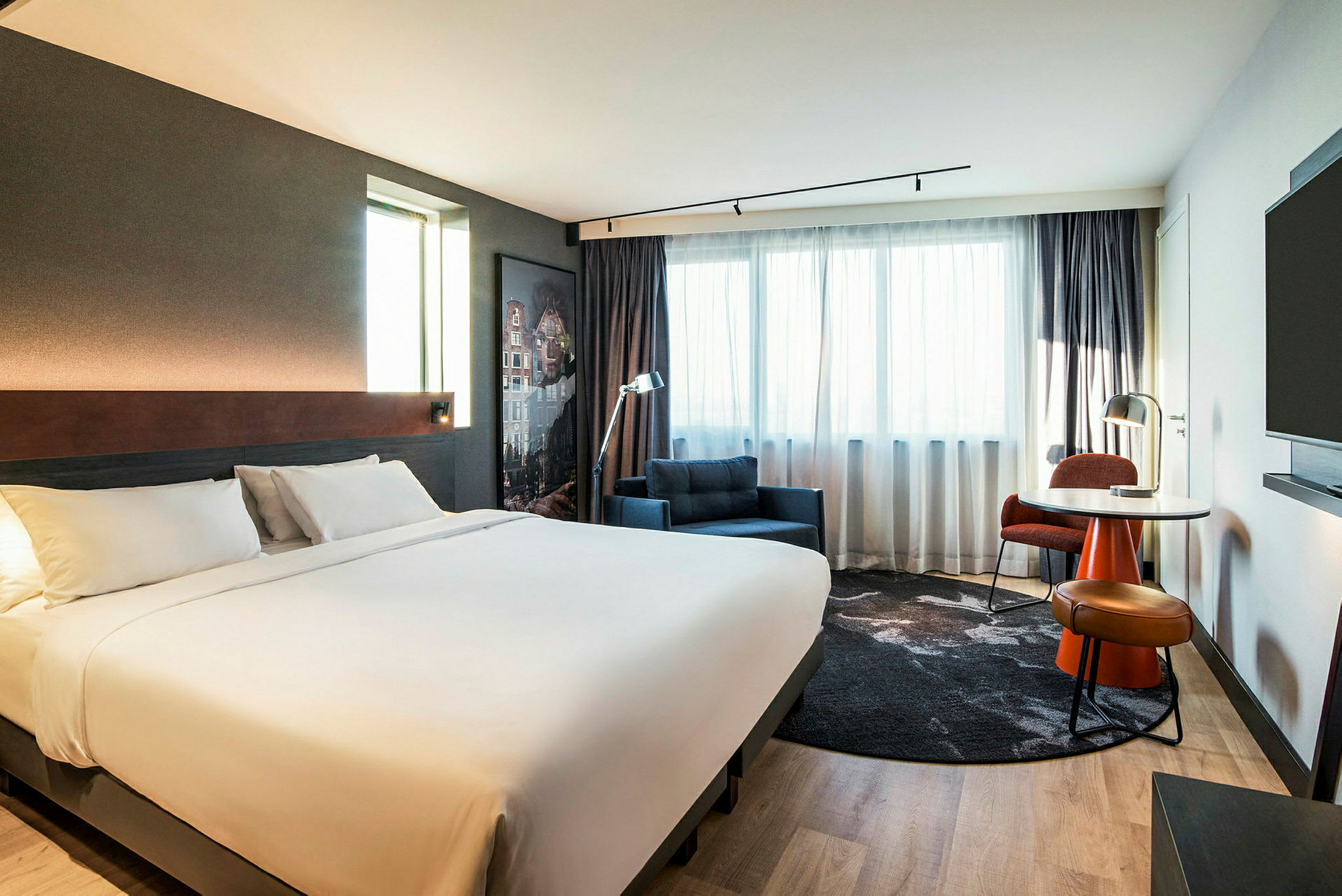 Ett modernt hotellrum med en stor dubbelsäng, fåtölj och ett skrivbord vid fönstret. (AI-genererad text)
