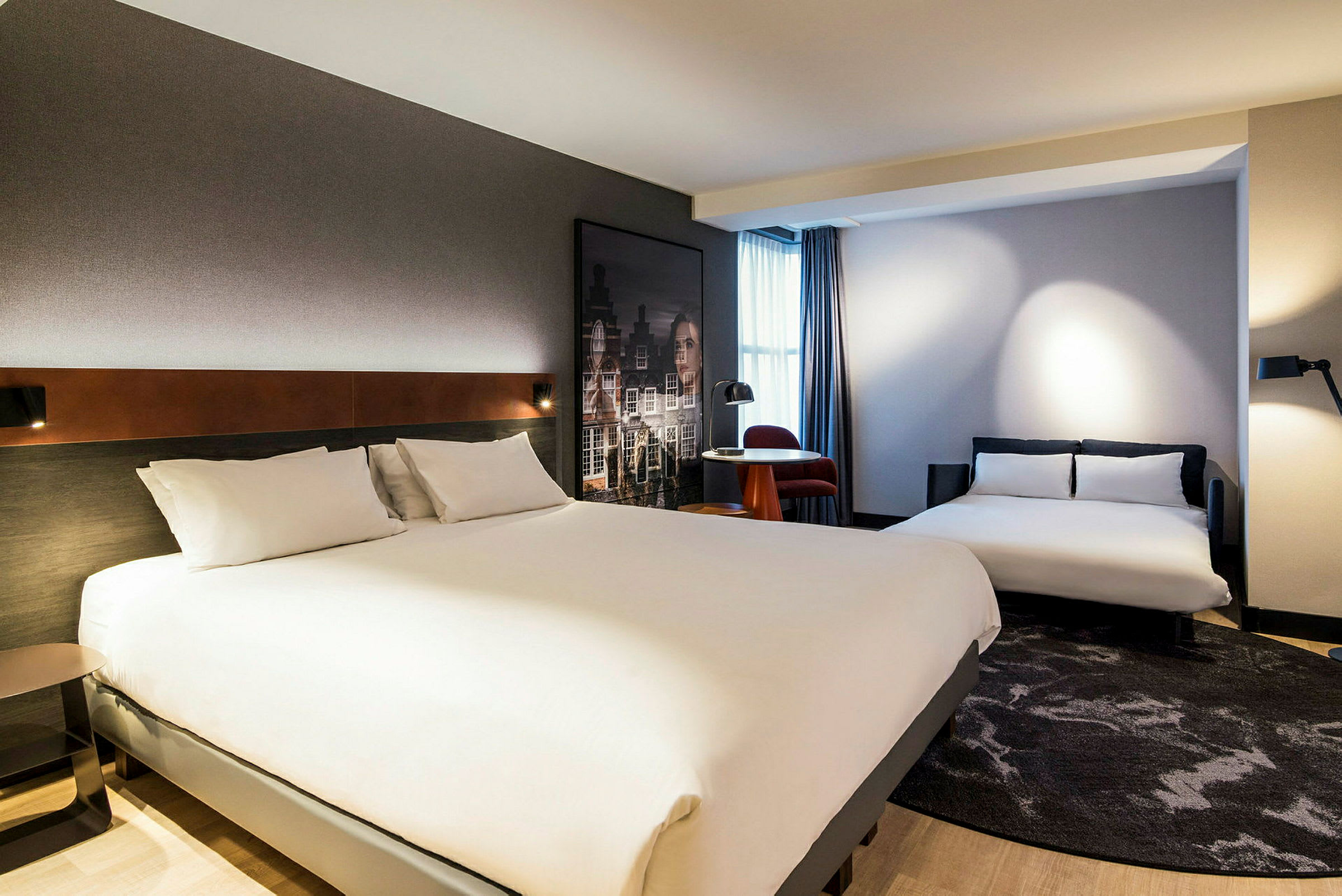 Hotellrum med två sängar och ett mindre bord med en stol vid ett fönster. (AI-genererad text)