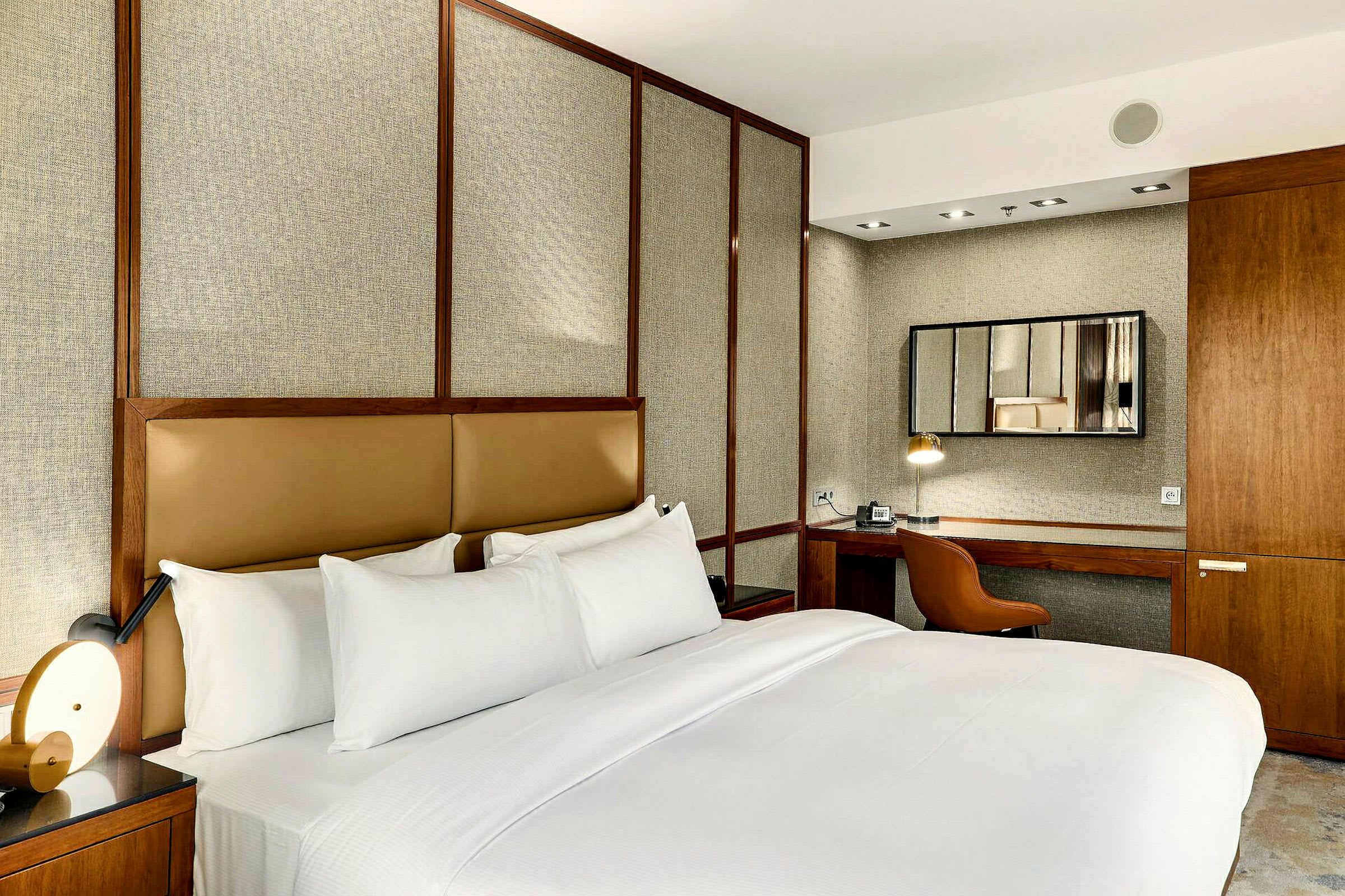 Ett elegant och stilrent hotellrum med en stor dubbelsäng, minimalistisk inredning och ett skrivbord med spegel. (AI-genererad text)
