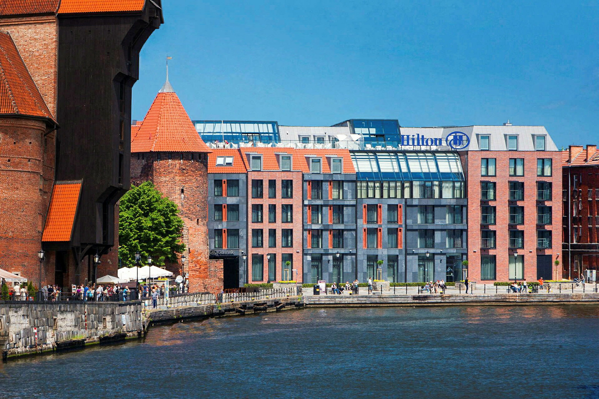 Ett vattendrag med byggnader i bakgrunden, inklusive ett hotell med modernt glasad fasad och historiska tegelkonstruktioner. (AI-genererad text)