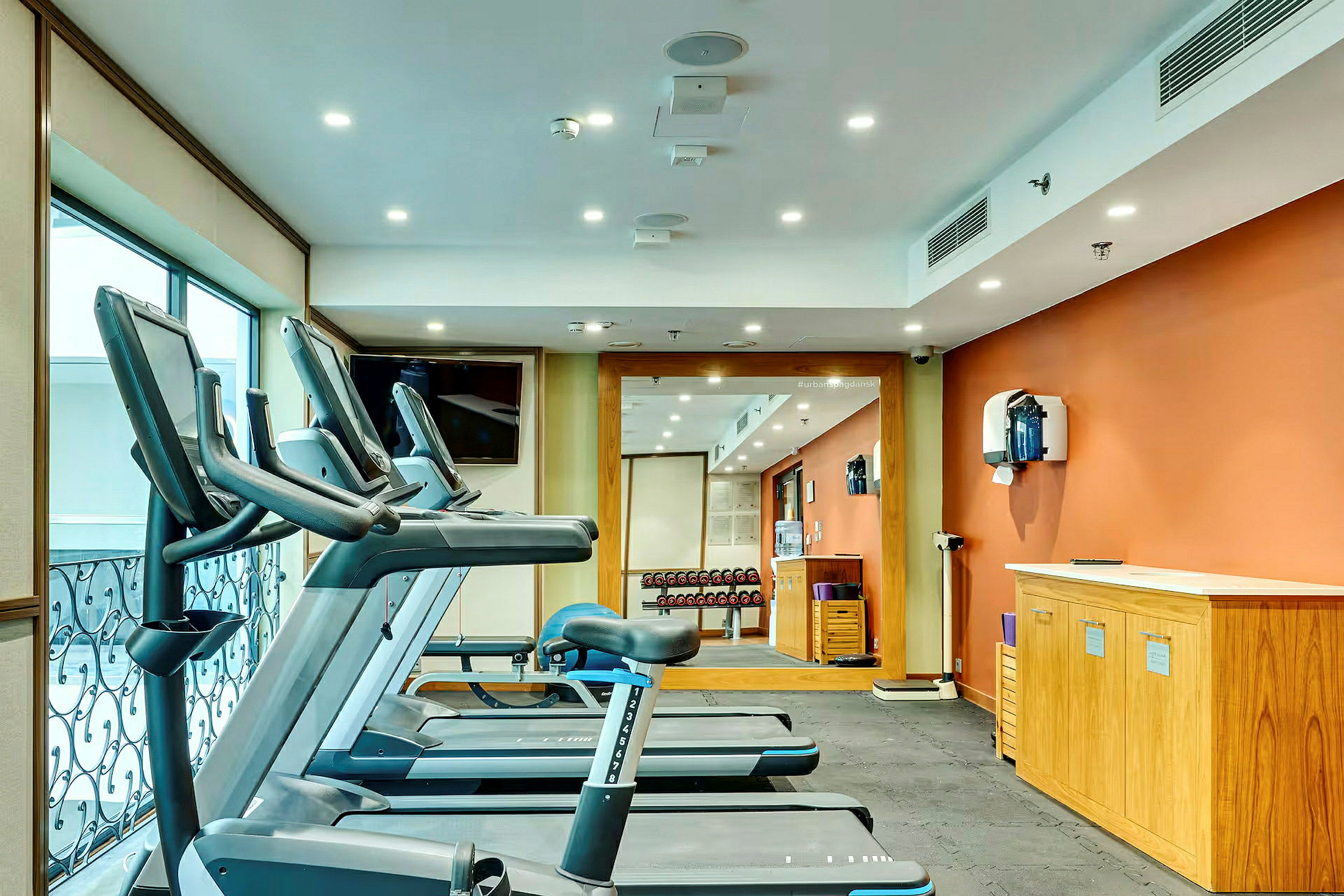 Ett gym med löpband, speglar och vikter längs en vägg. (AI-genererad text)