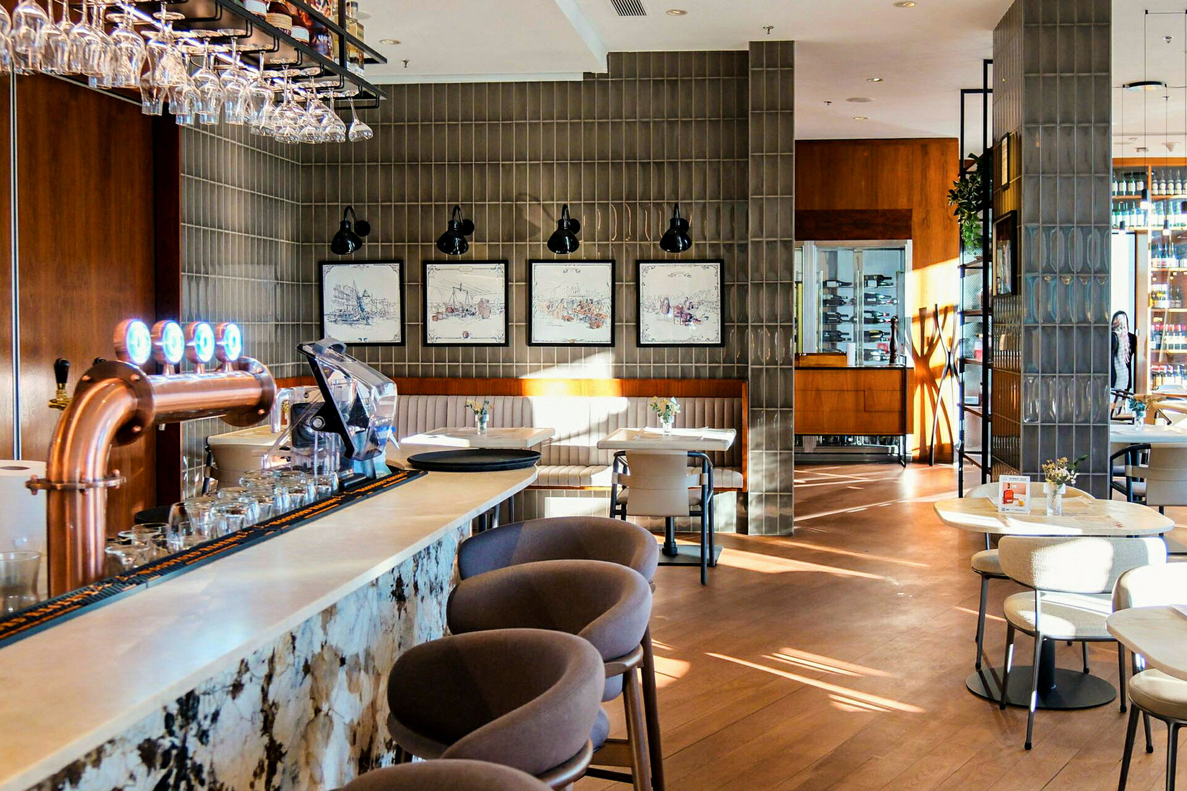 En stilren restauranginteriör med en bardisk i förgrunden, stolar och bord spridda runt lokalen samt dekorationer och växter. (AI-genererad text)