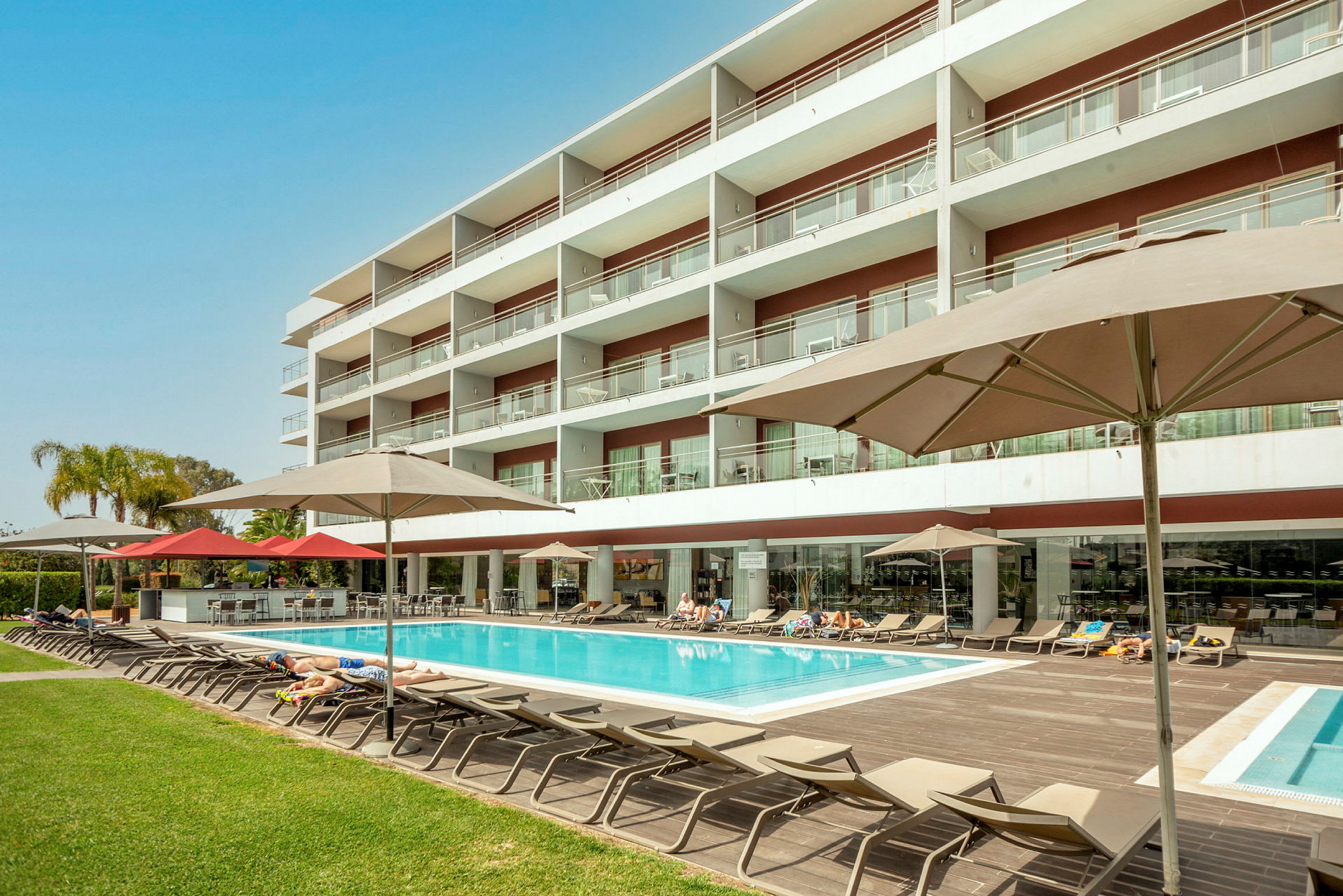 Hotellbyggnad med pool och solstolar. (AI-genererad text)