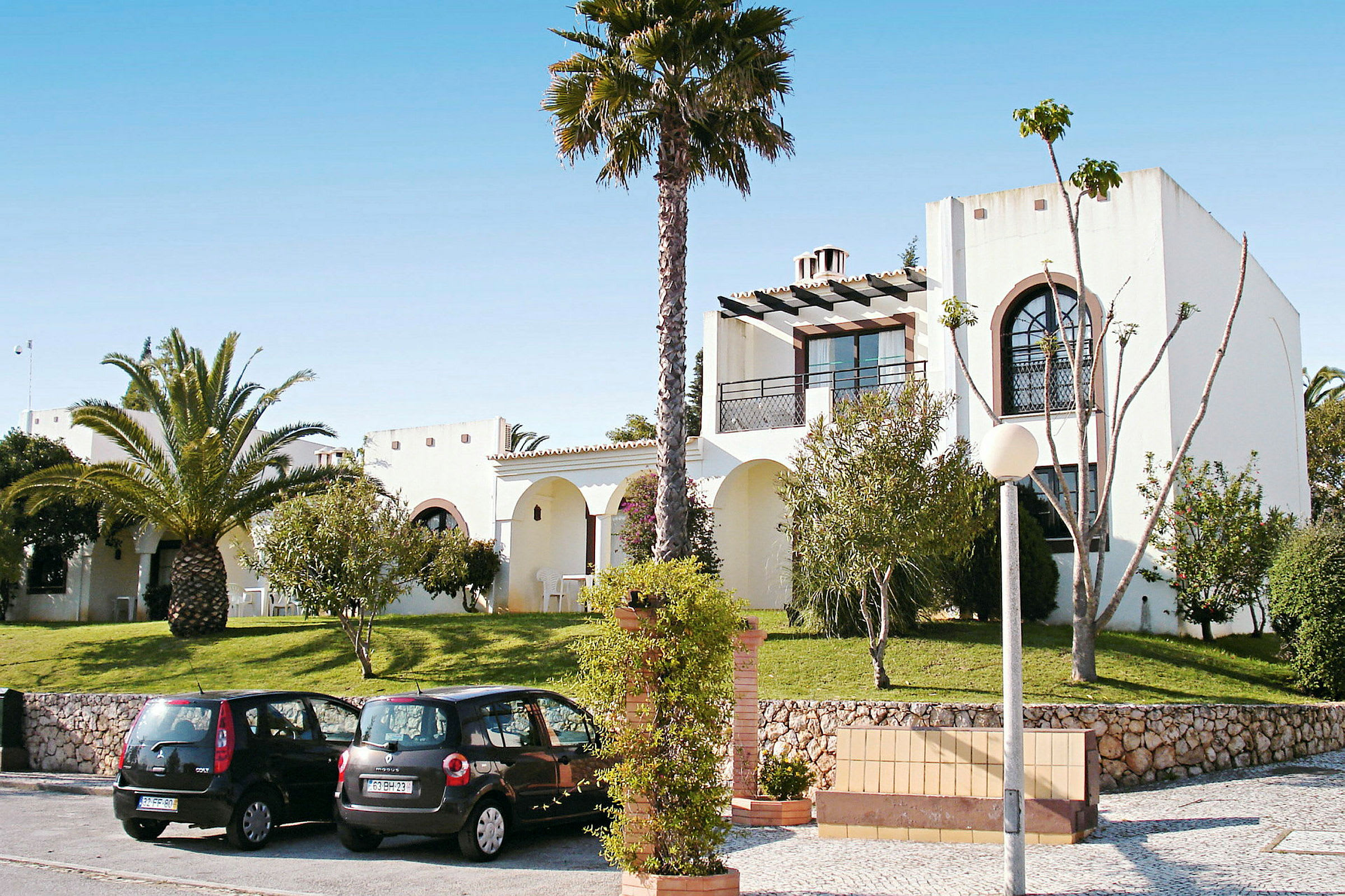 Bild av vit villa med palmträd och parkerade bilar framför. (AI-genererad text)