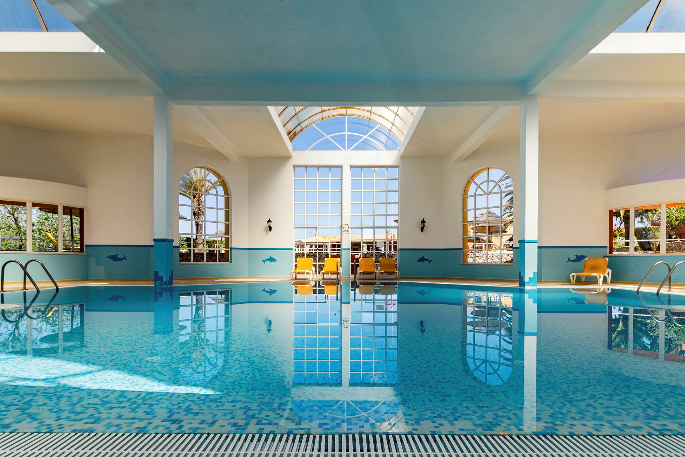 Inomhuspool med stora fönster, solsängar och dekorativa väggmålningar. (AI-genererad text)