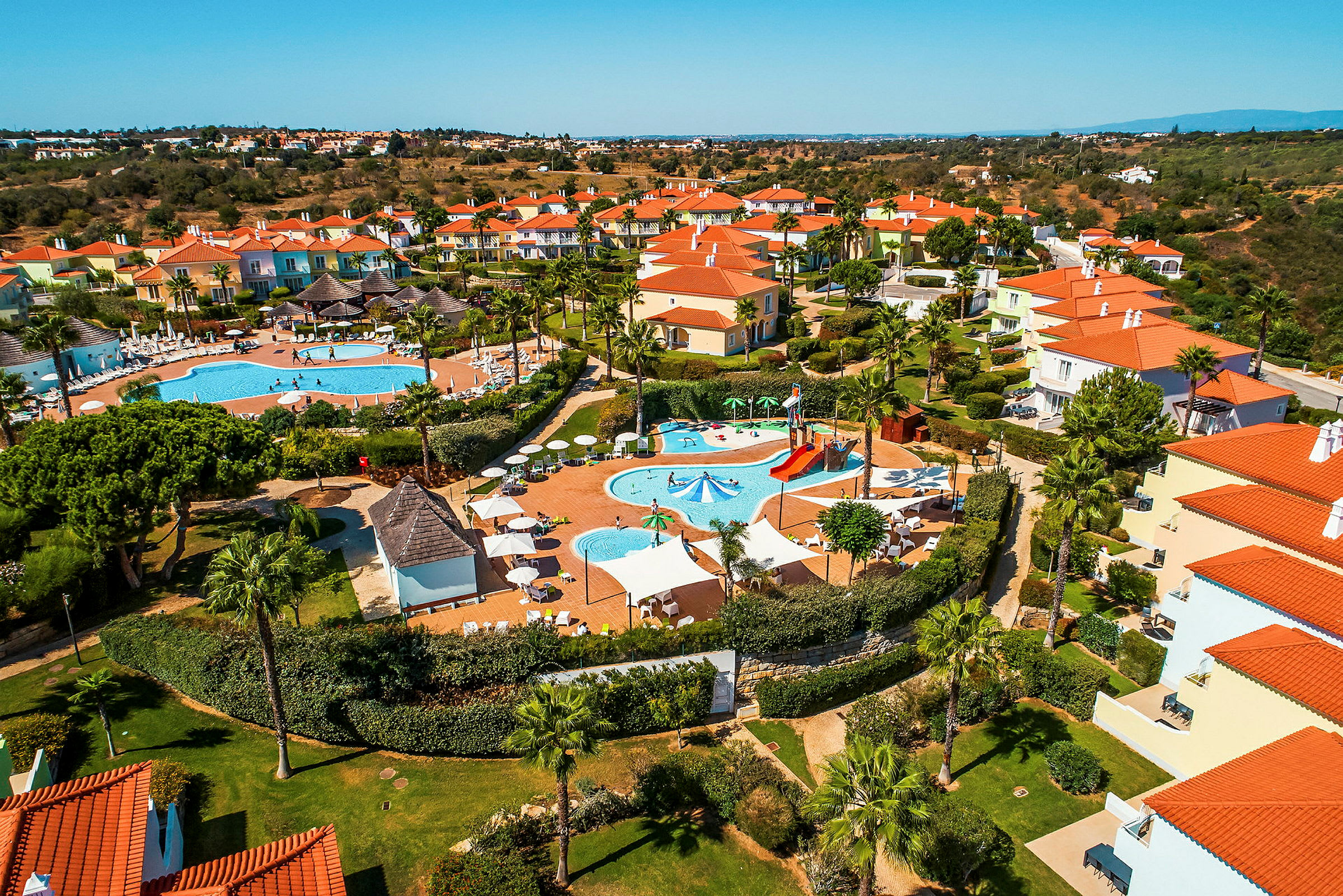 Flygfoto över ett semesterkomplex med pooler och färgglada hus. (AI-genererad text)