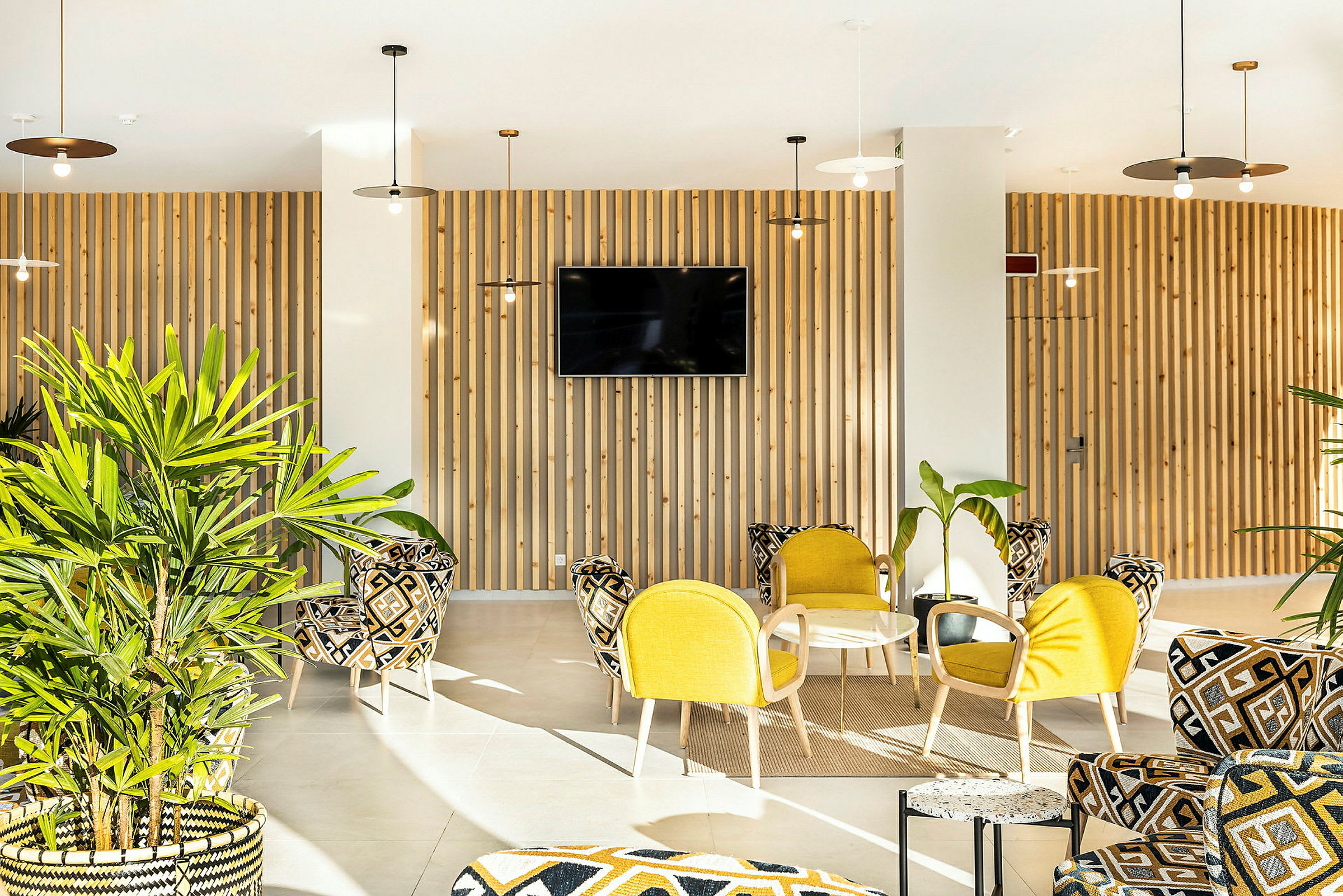 En ljus och modern lounge med gul och mönstrad möblering samt gröna växter. (AI-genererad text)