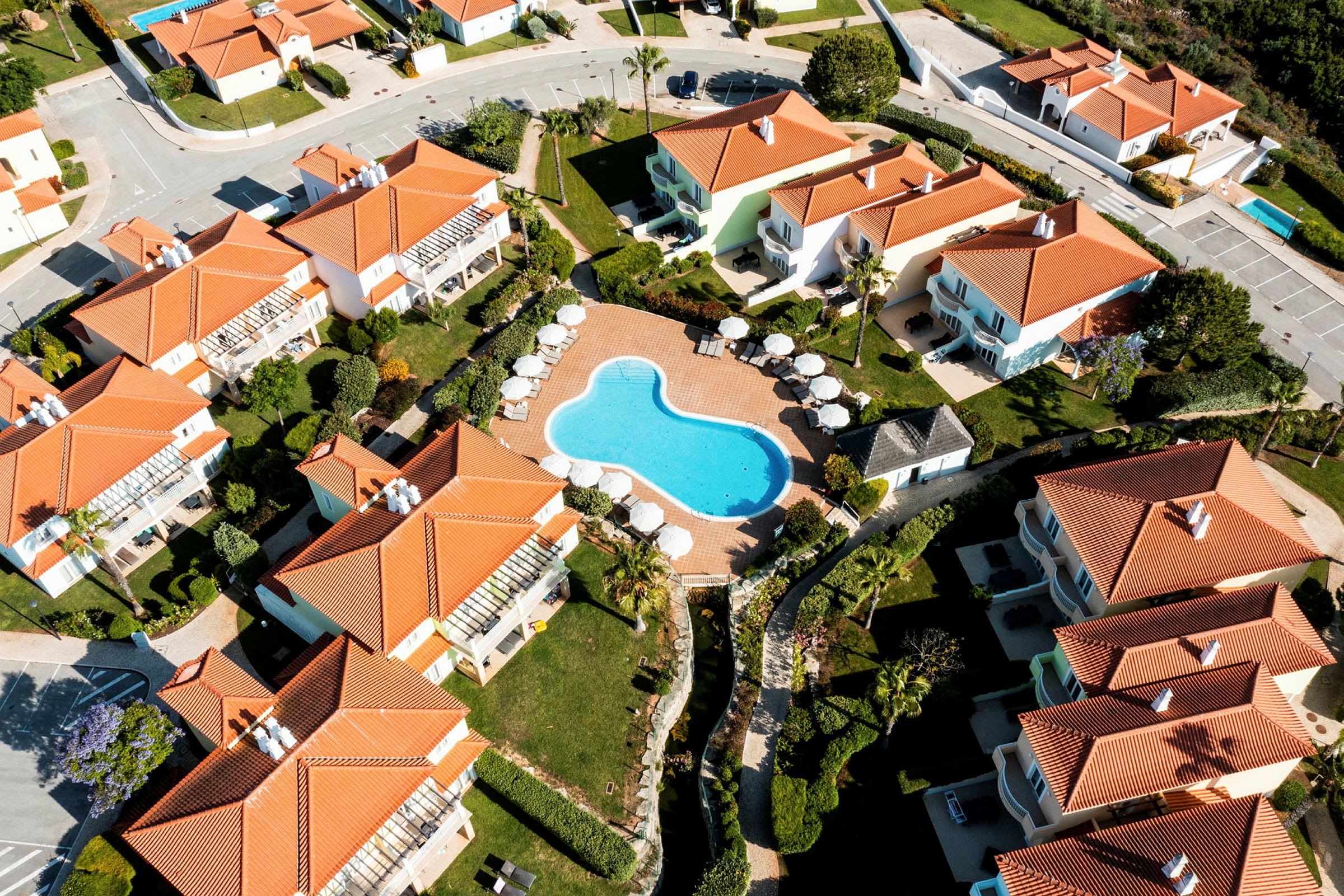 Flygbild över semesterhus med röda tak kring en pool. (AI-genererad text)